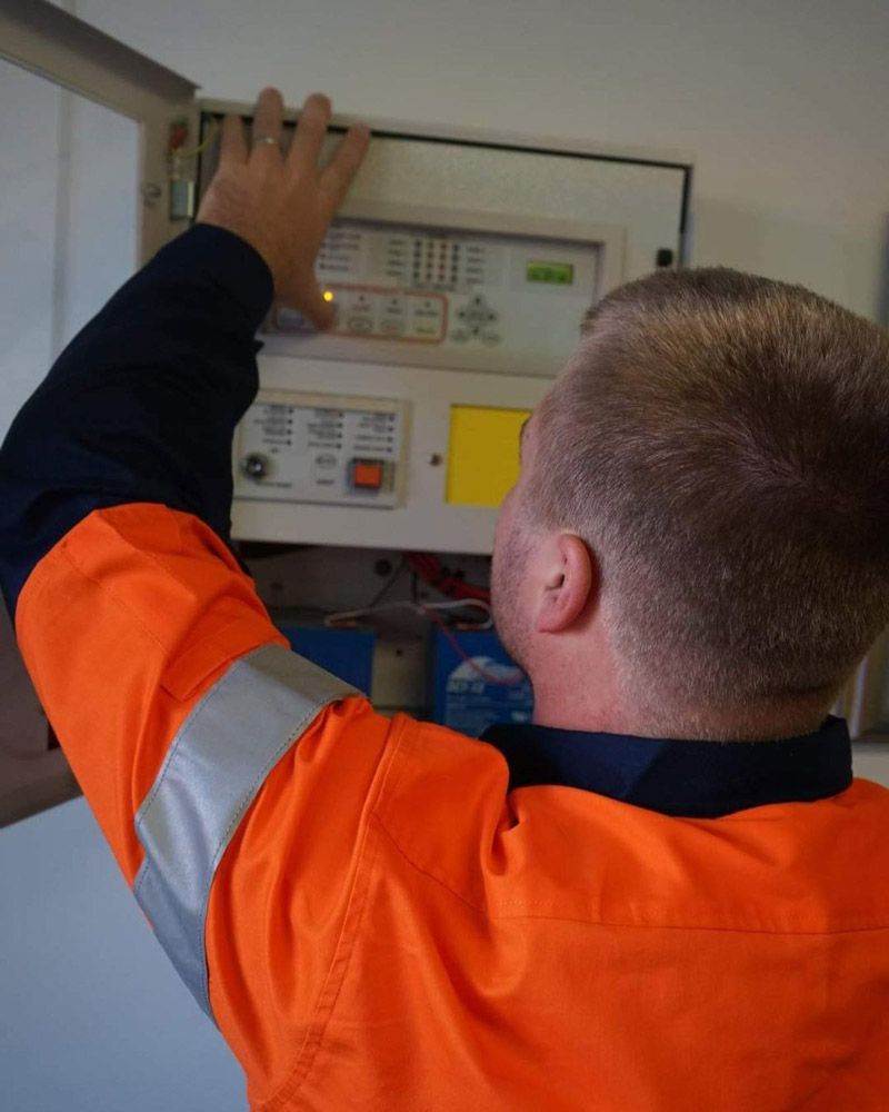 A Man In An Orange Jacket Is Working On A Control Panel — Firewerx In Bathurst, NSW