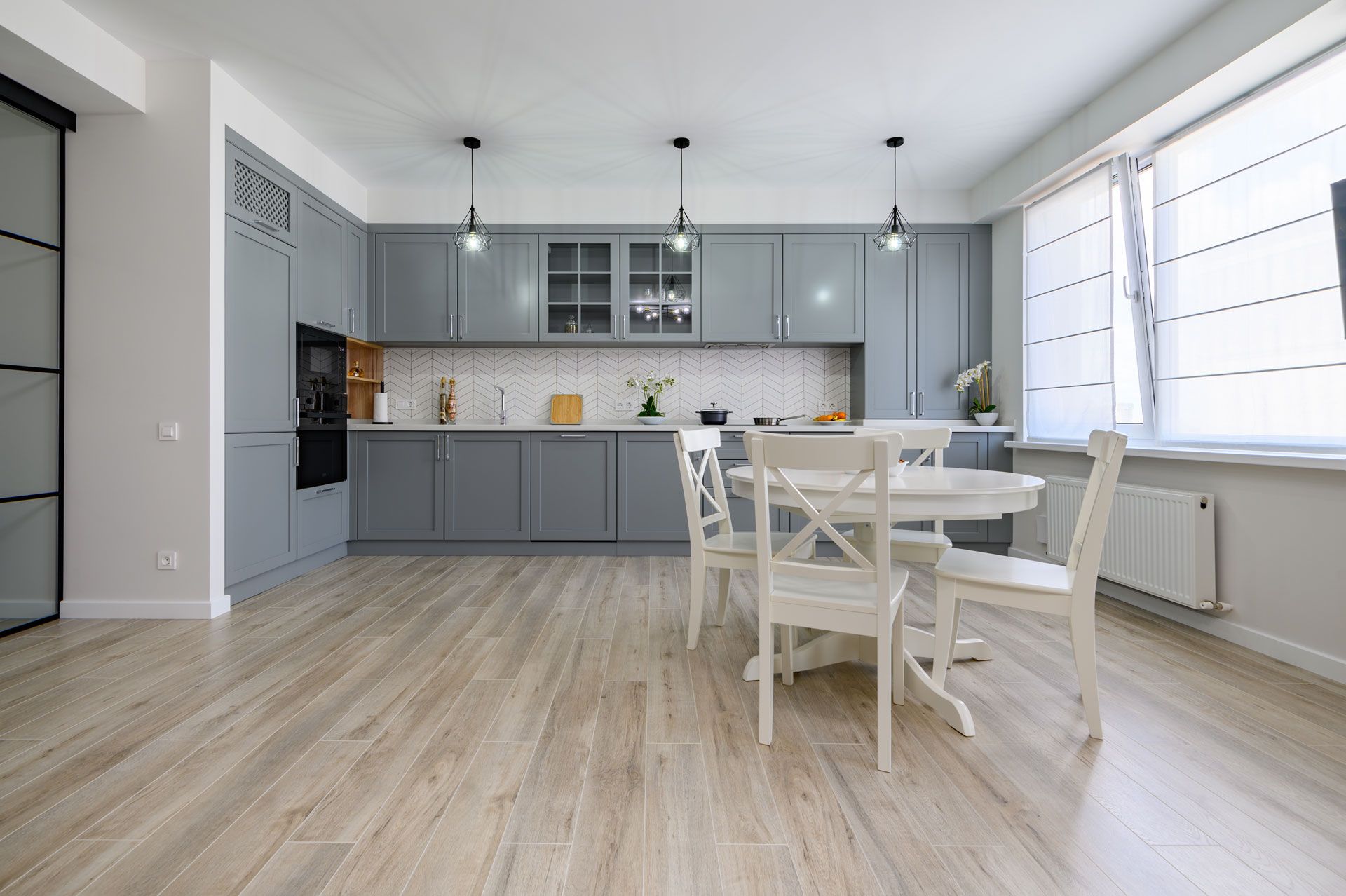 Gray kitchen with light wood floor, cabinets, and a white round table with chairs.
