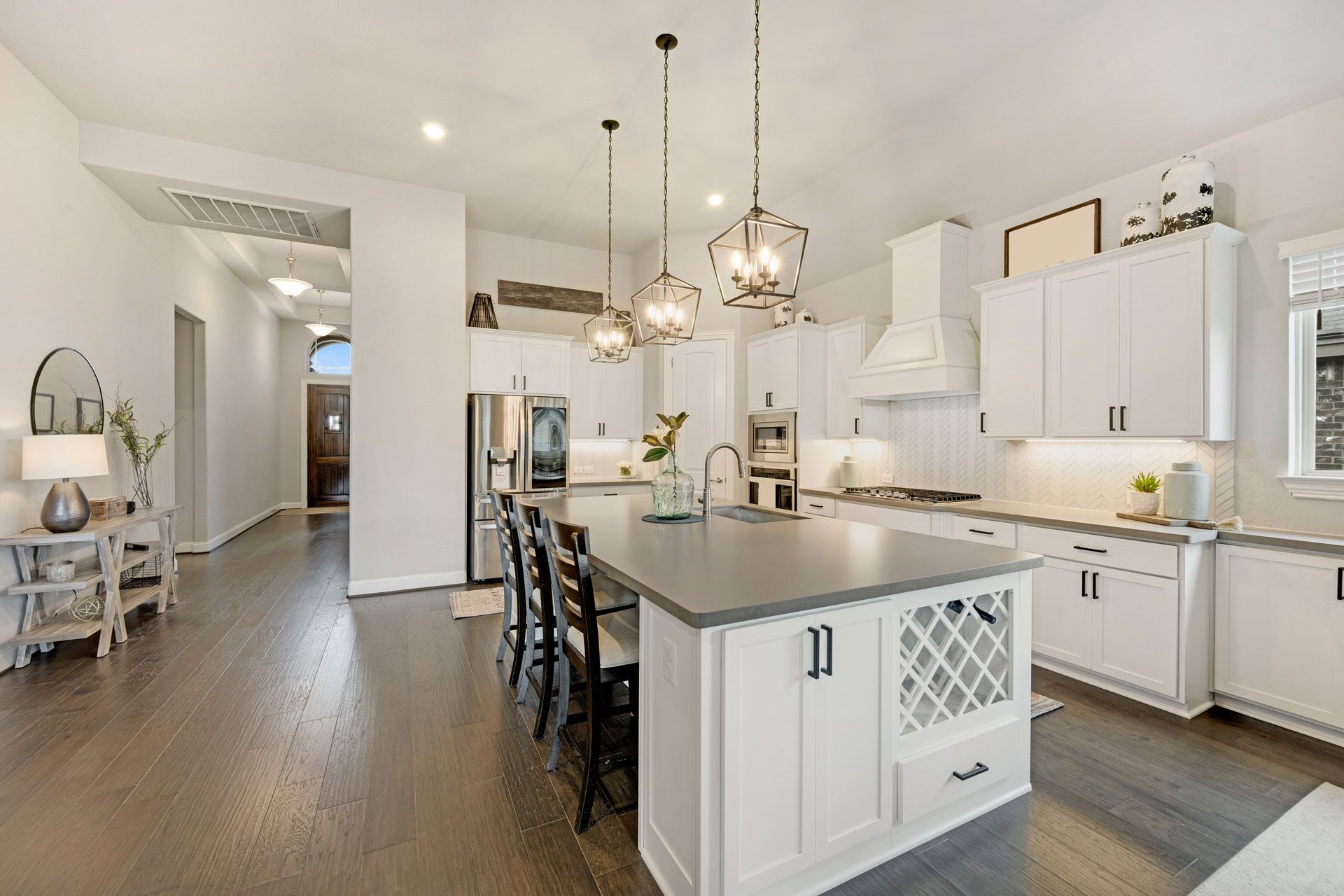 Modern kitchen with white cabinets, dark wood floors, large island, and pendant lights.