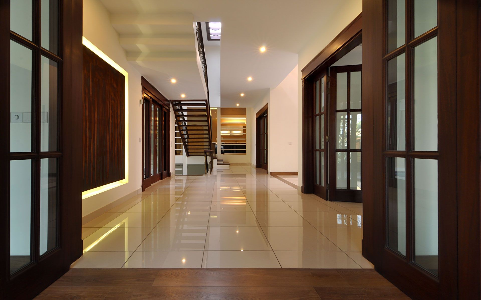 Hallway with wood-framed glass doors, glossy tile floor, and a staircase leading to the upper level.