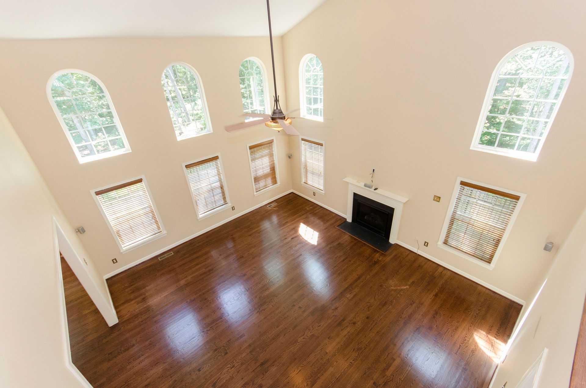 View from above of a large living room with dark wood floors, arched windows, and a fireplace.
