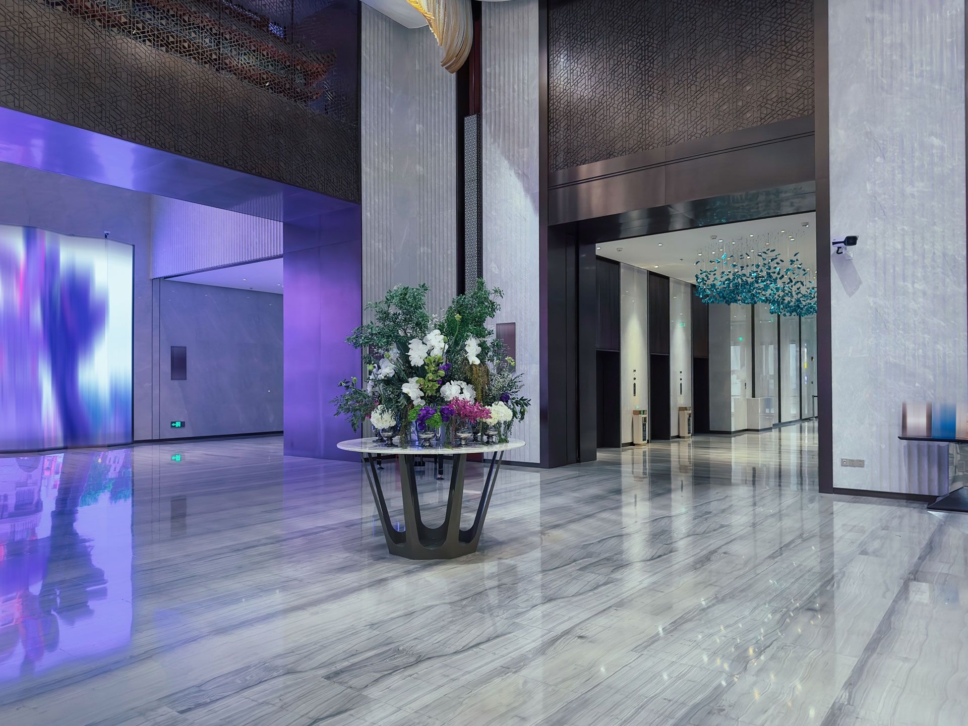 Lobby with marble floor, floral arrangement, and elevators. Blue and purple lighting. Modern design.