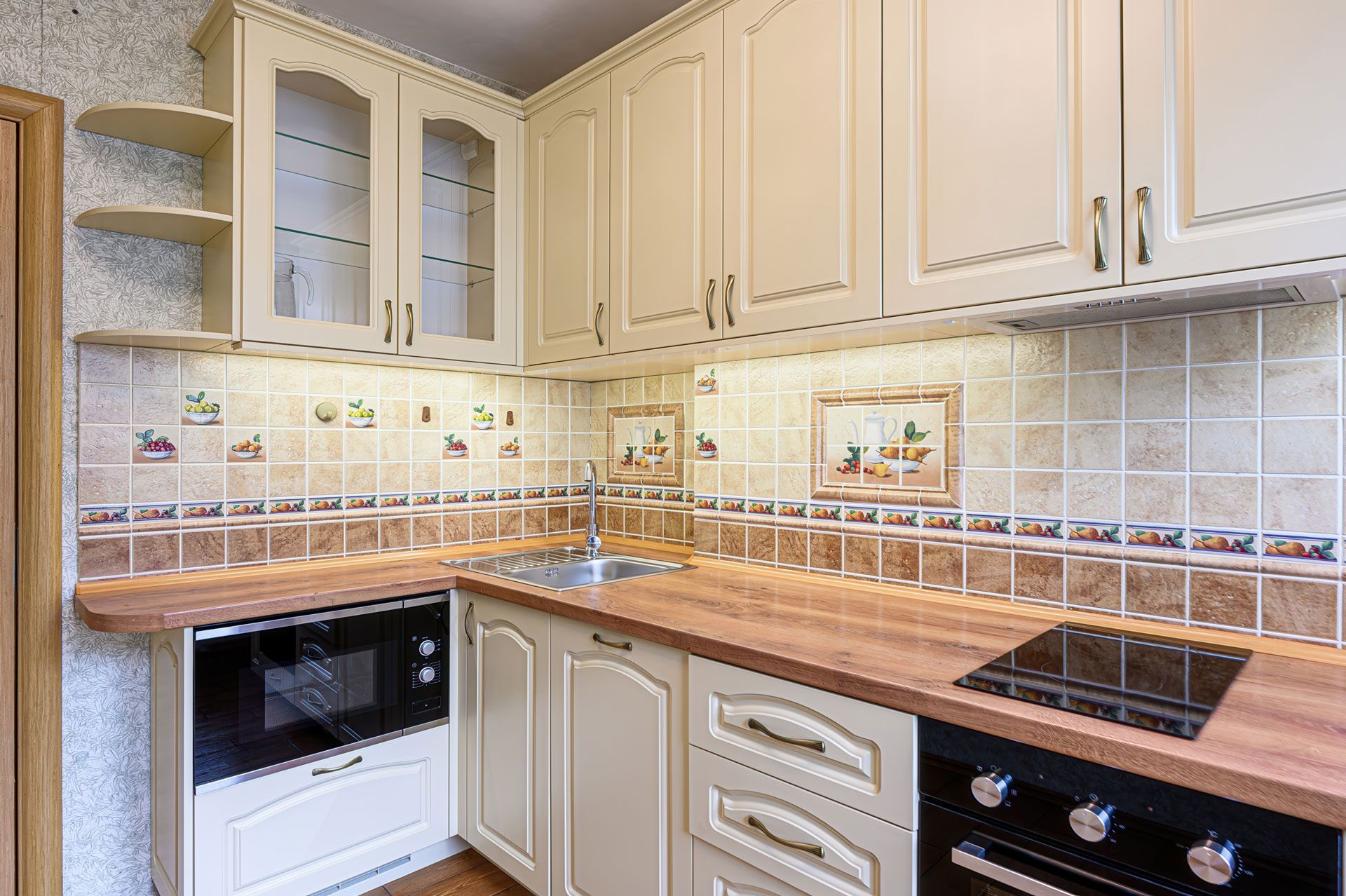 Beige kitchen with upper cabinets, countertop, and appliances. Tile backsplash.
