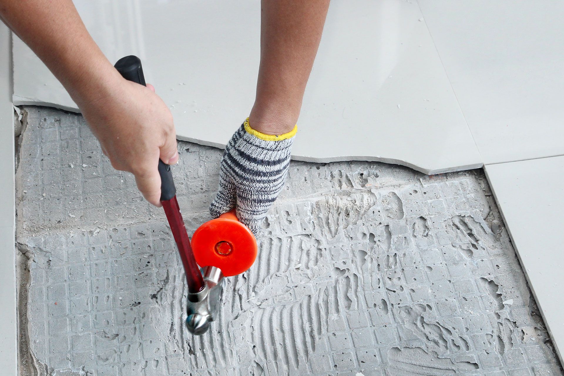 Person using a hammer and a tile-setting tool to remove floor tile.