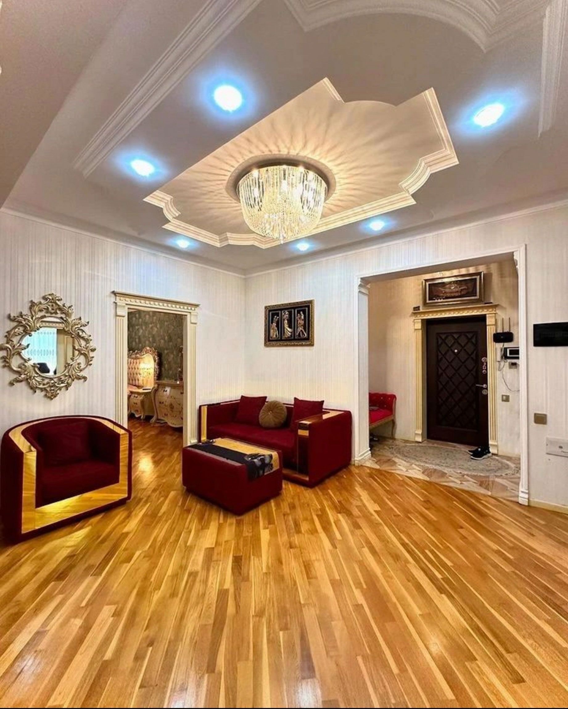 Living room with red furniture, gold accents, ornate ceiling, and wooden floors.