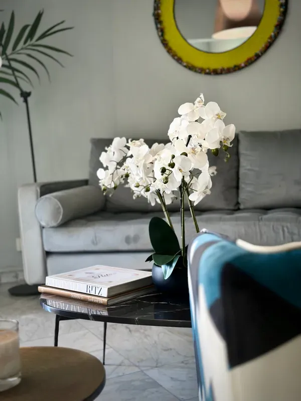 Un salon avec un canapé une chaise un livre et un vase de fleurs