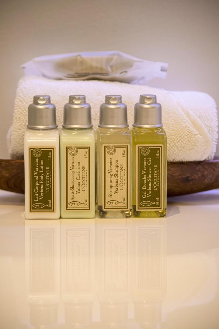 Quatre bouteilles de lotion sont posées sur un plateau en bois à côté d'une serviette.