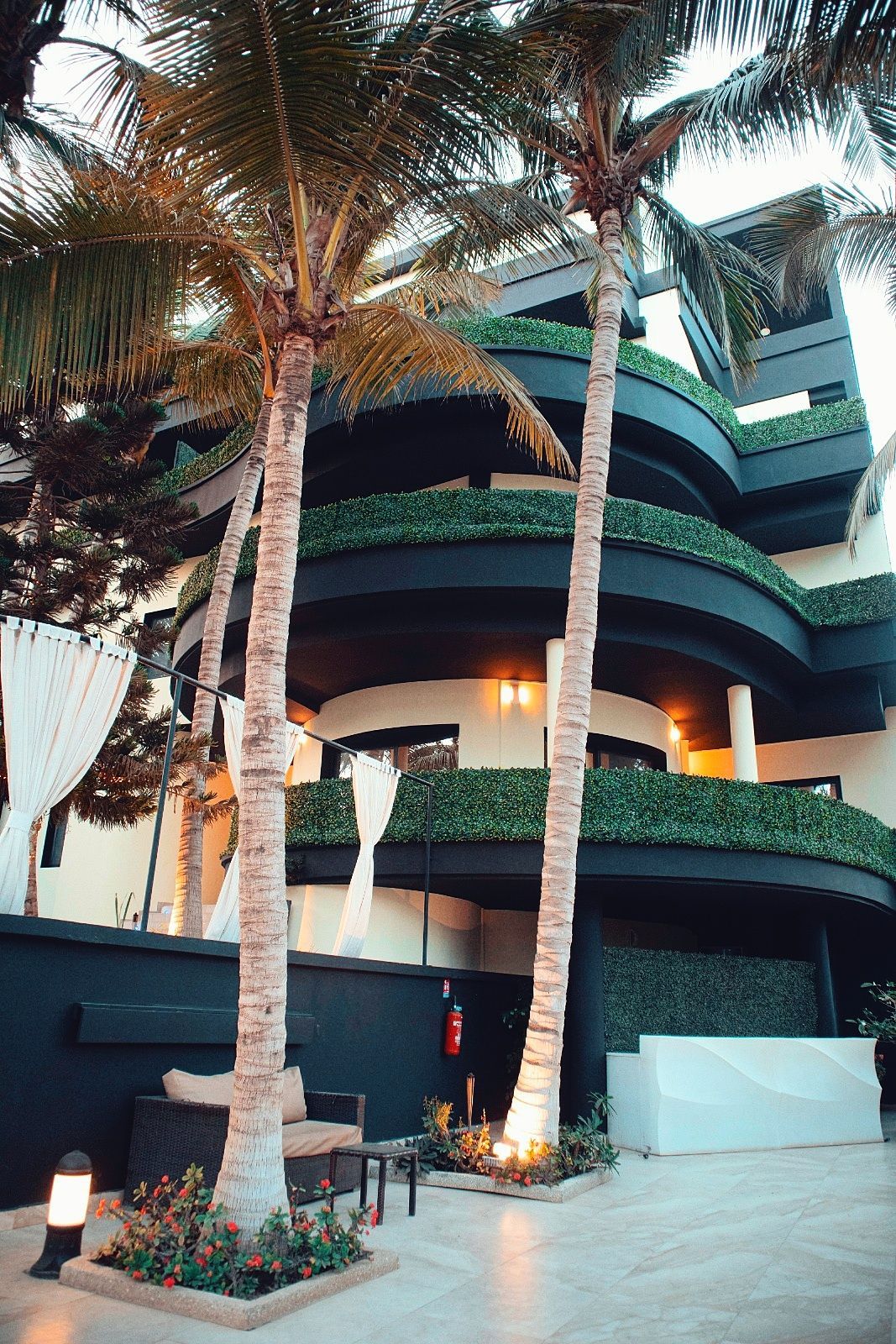 Un grand bâtiment avec beaucoup de balcons et de palmiers devant.