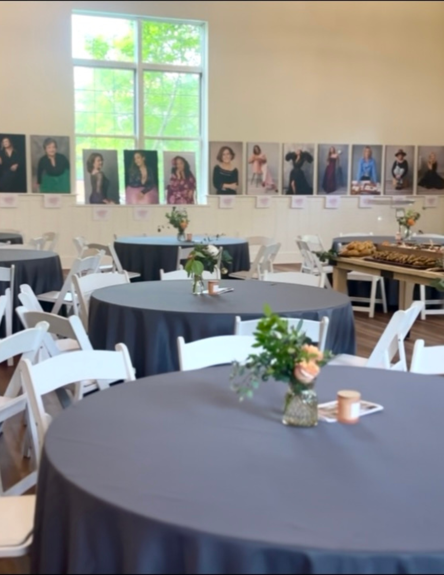 Event space with round tables, flowers, portraits on the wall, and white folding chairs.