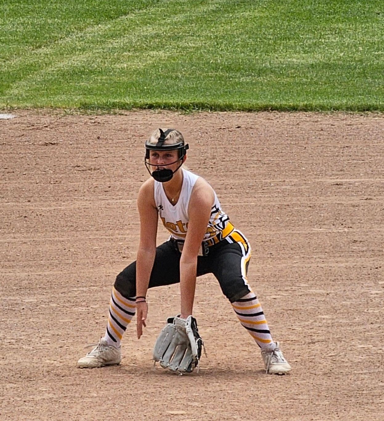 A woman is kneeling on a baseball field holding a glove.