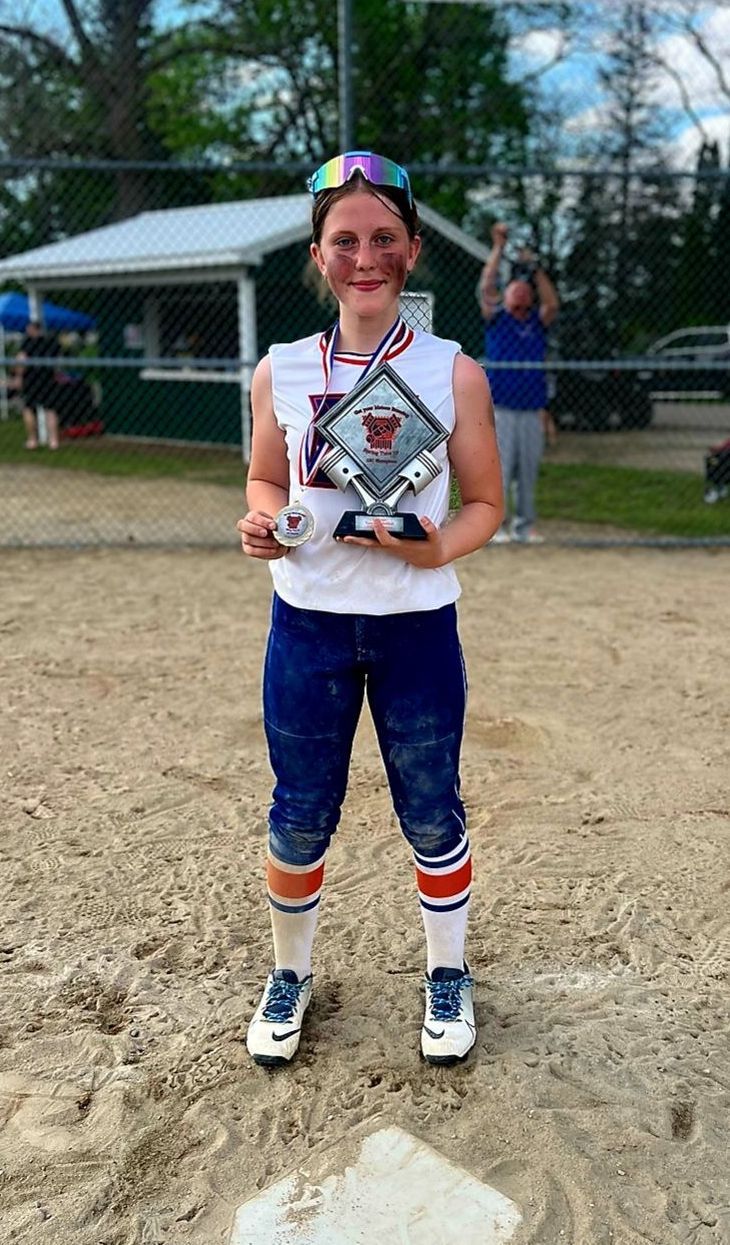 A young girl is standing on a baseball field holding a trophy.
