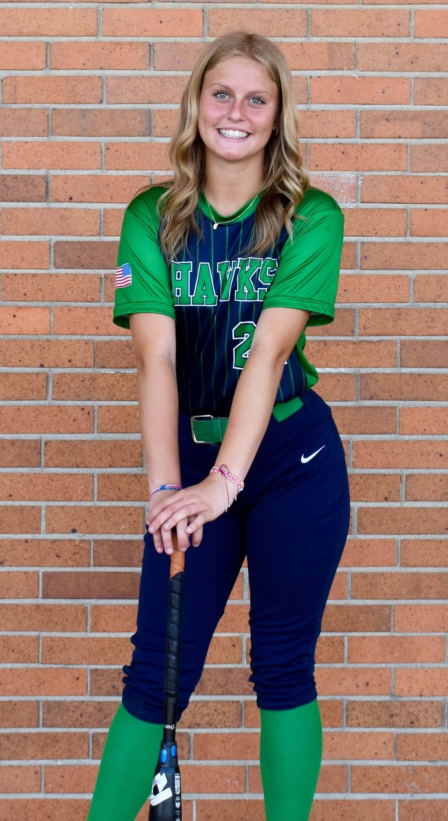 A girl in a green and blue softball uniform is holding a bat.