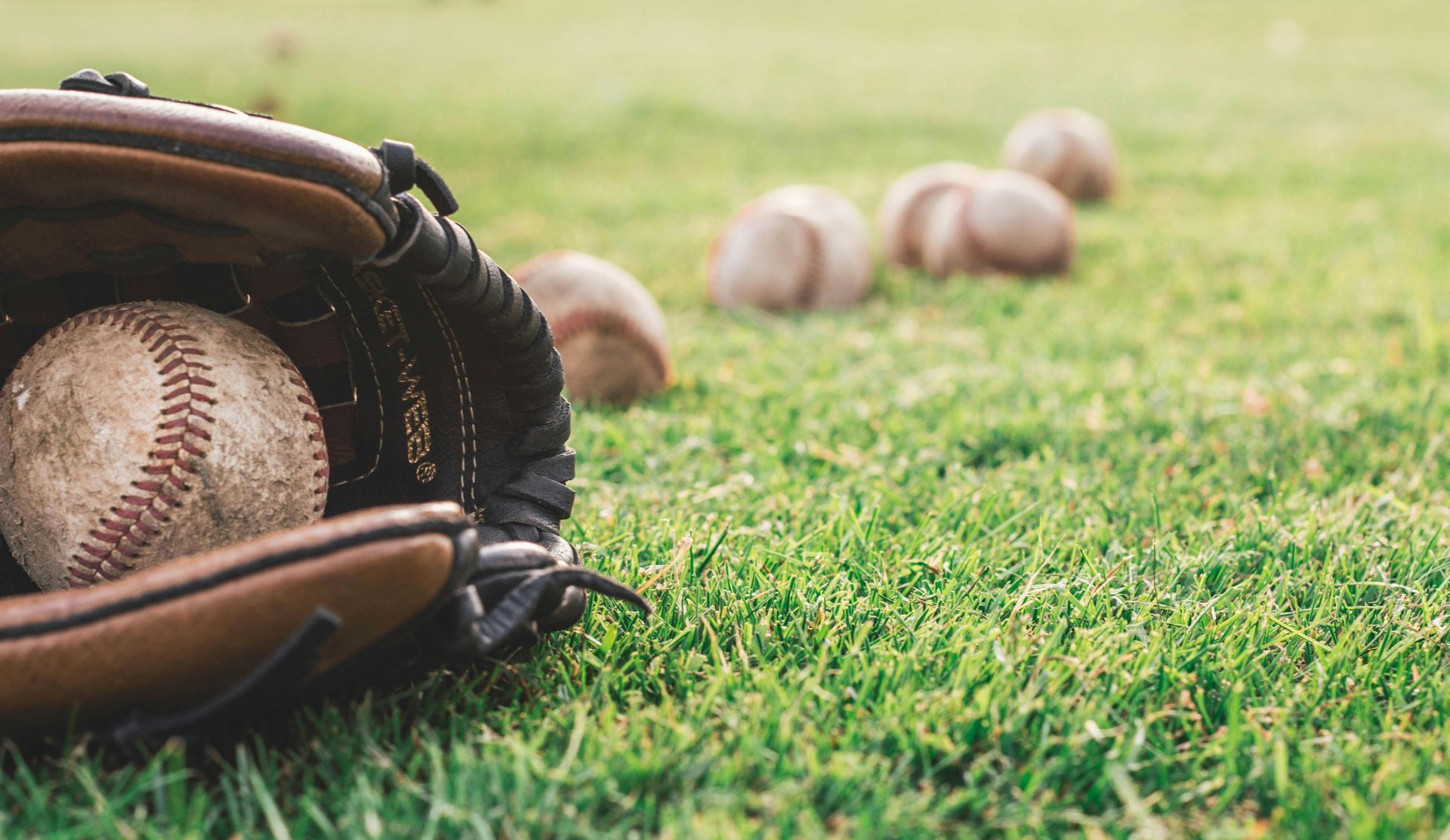 A baseball glove with a baseball in it is laying on the grass. Softball and baseball training