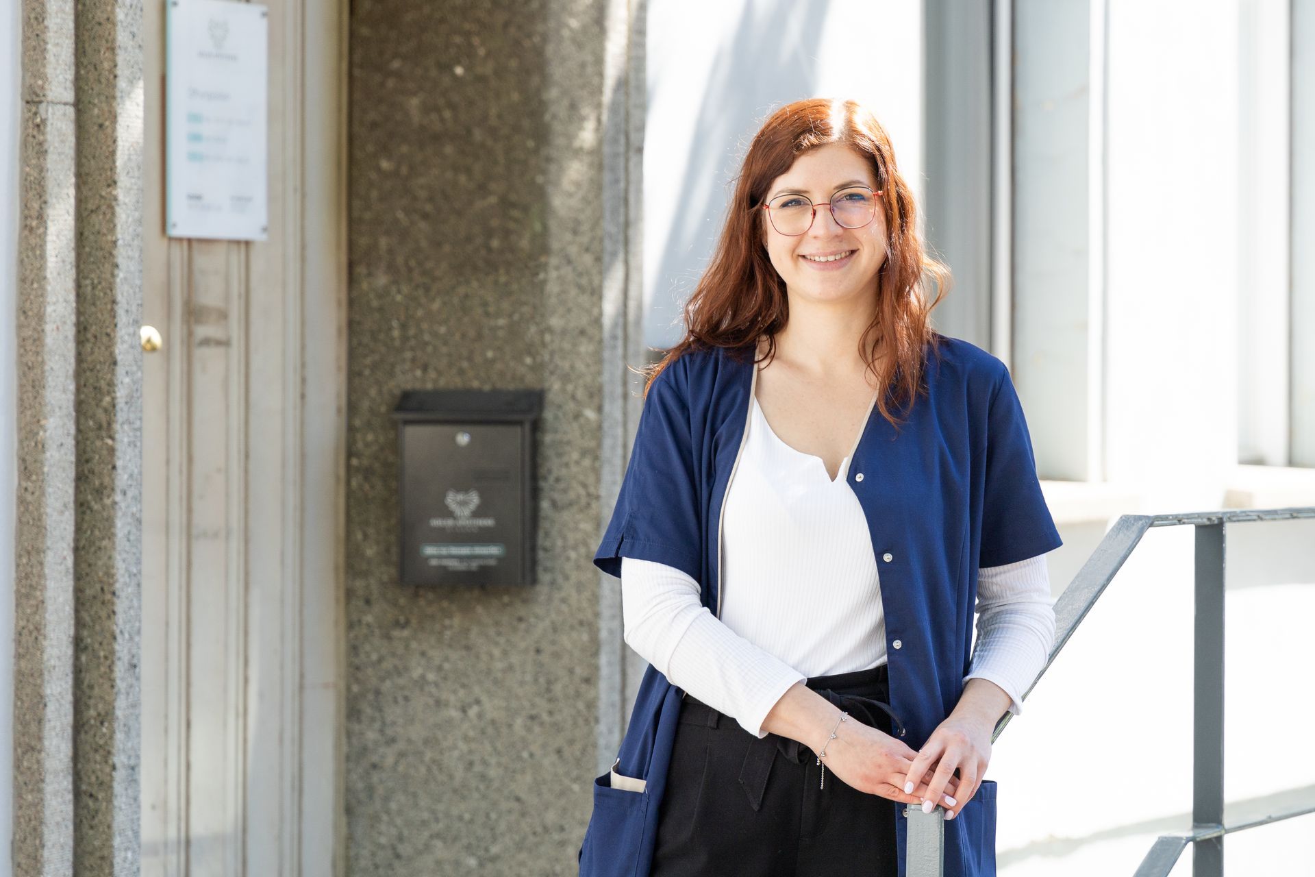 Eine Frau in einem blauen Mantel steht vor einem Gebäude.