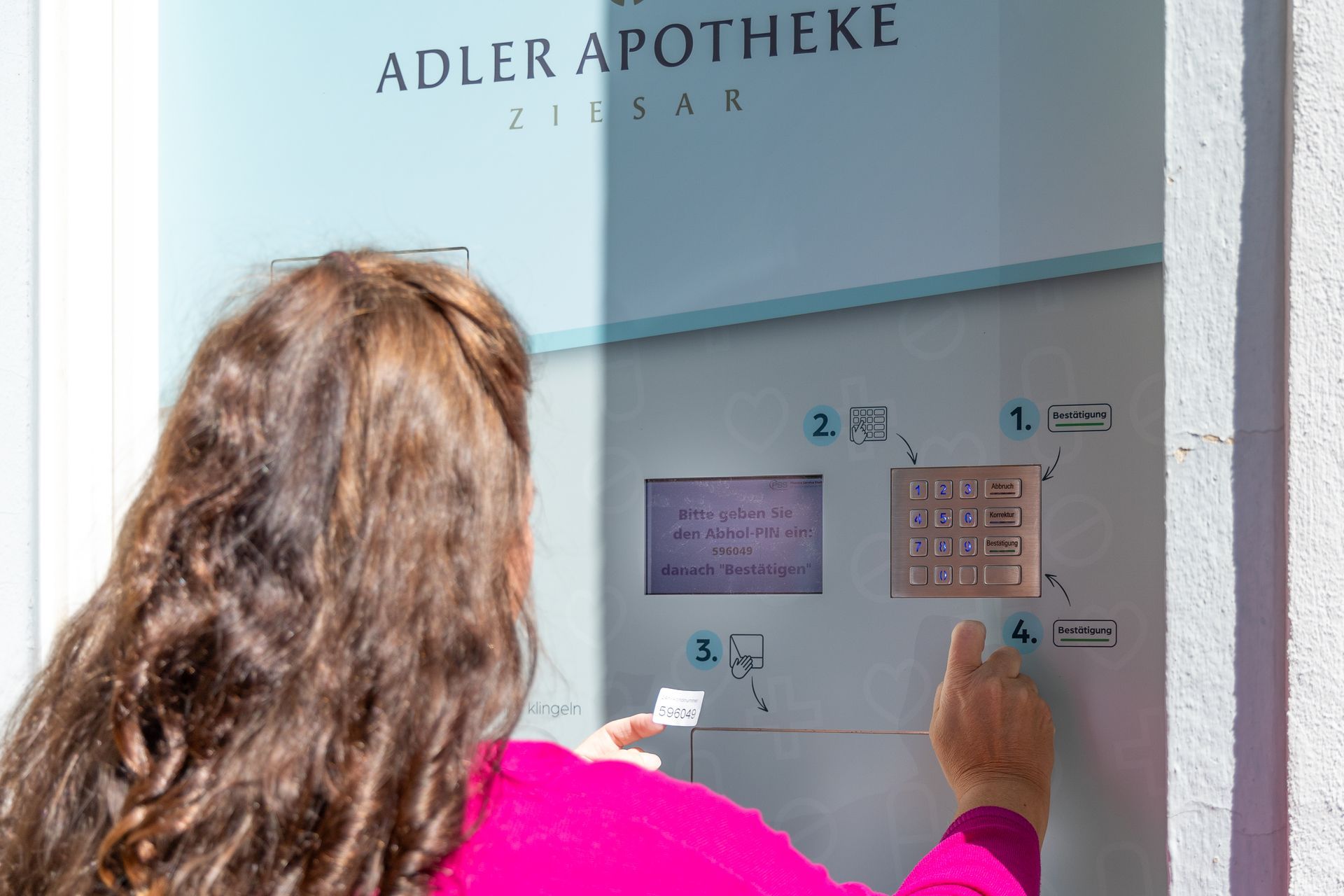 Eine Frau in einem rosa Hemd benutzt in einer Apotheke einen Automaten.