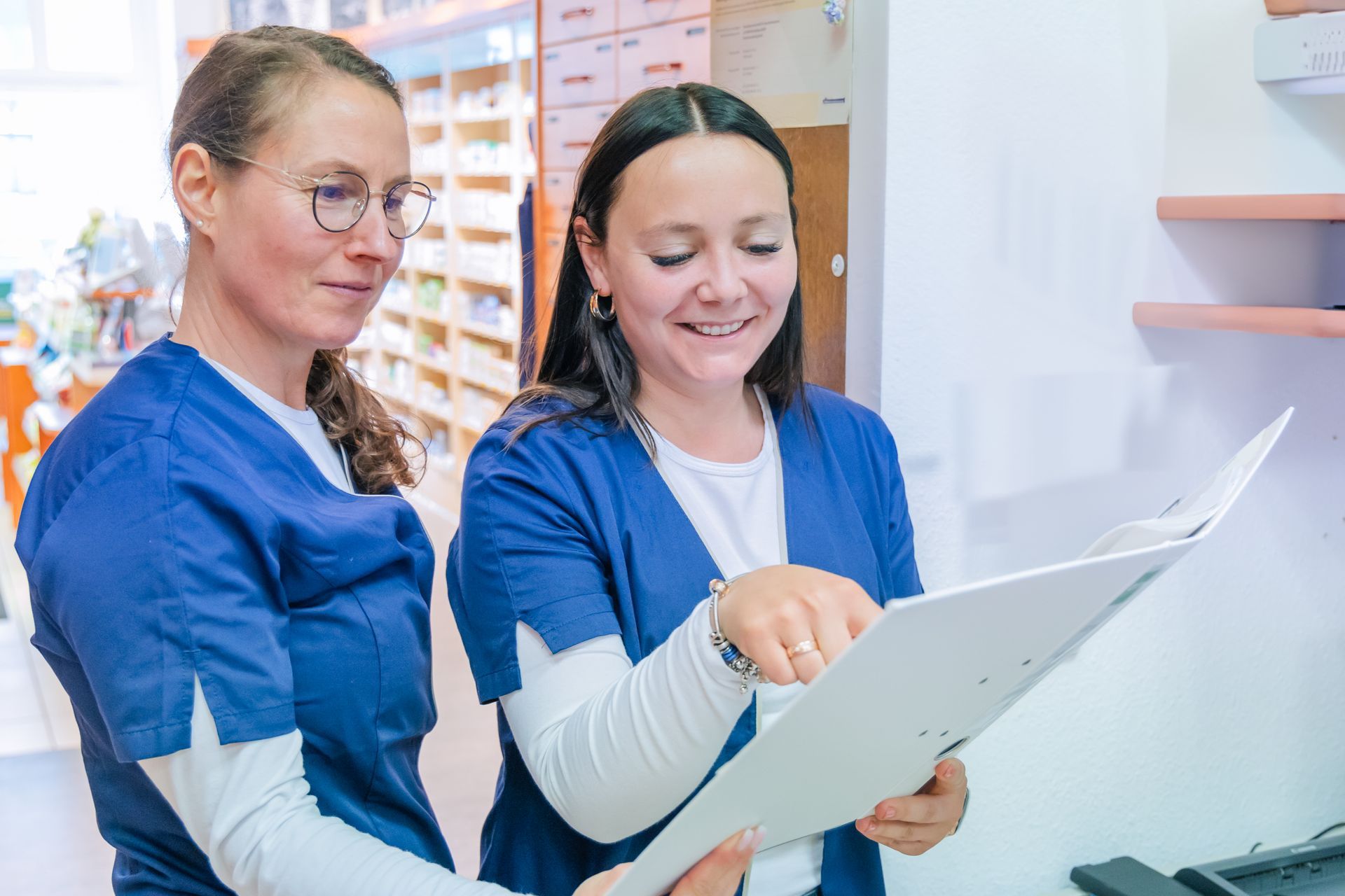 Zwei Krankenschwestern schauen sich in einer Apotheke einen Ordner an.