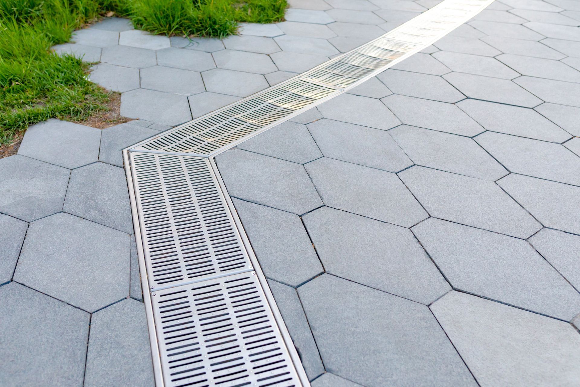 A drain on the side of a brick walkway with grass in the background.