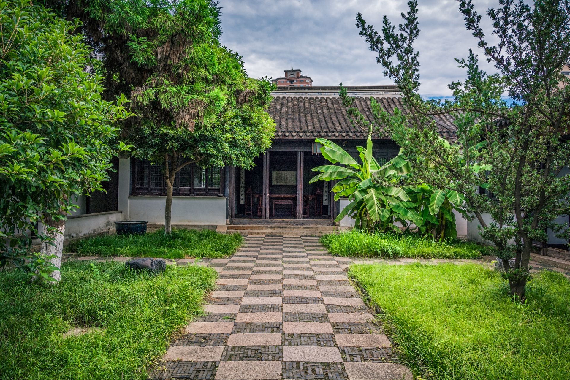 A house with a checkered walkway leading to it surrounded by trees and grass.