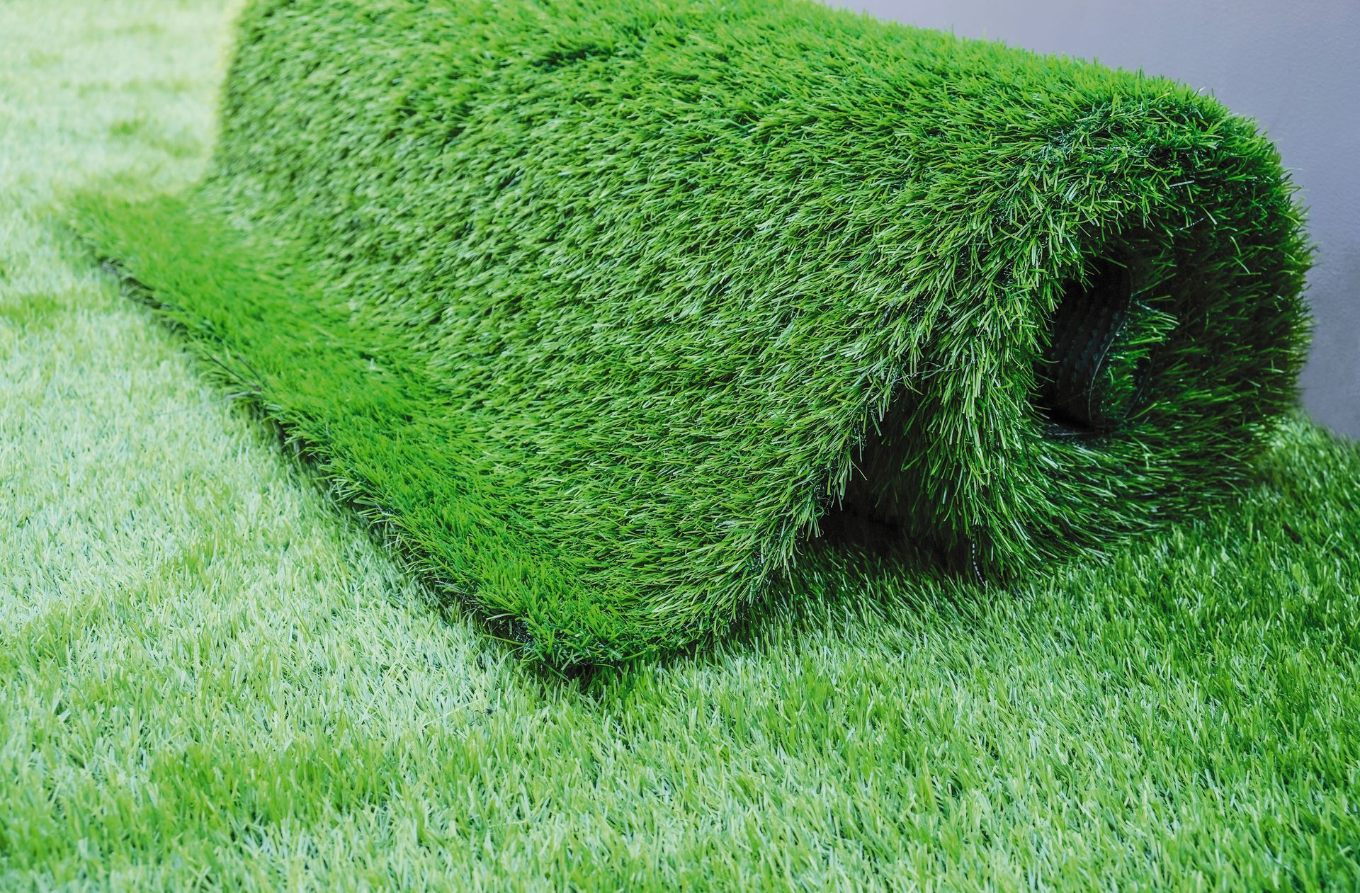 A roll of green artificial grass is sitting on top of a carpet.