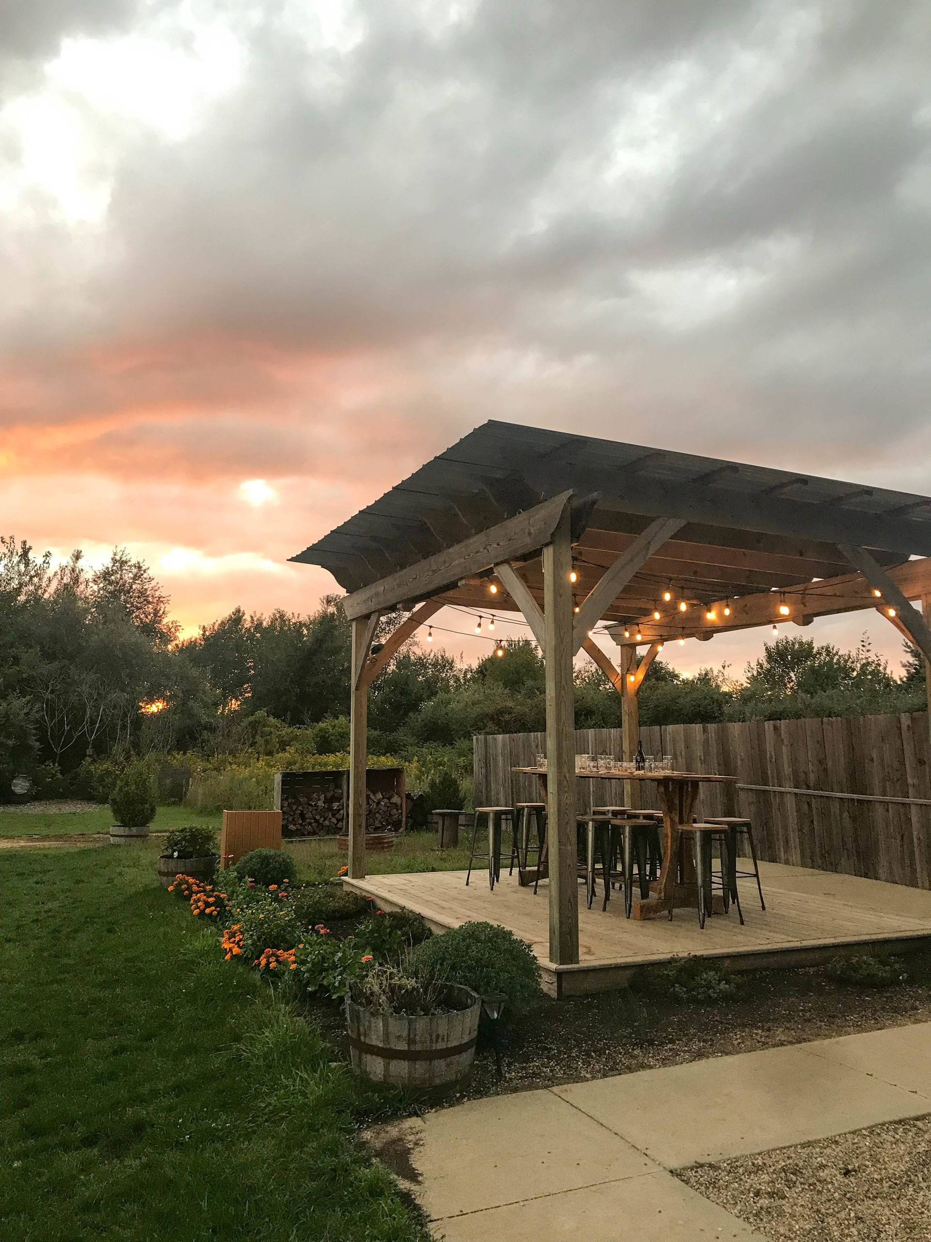 A wooden gazebo with tables and stools underneath it at sunset.