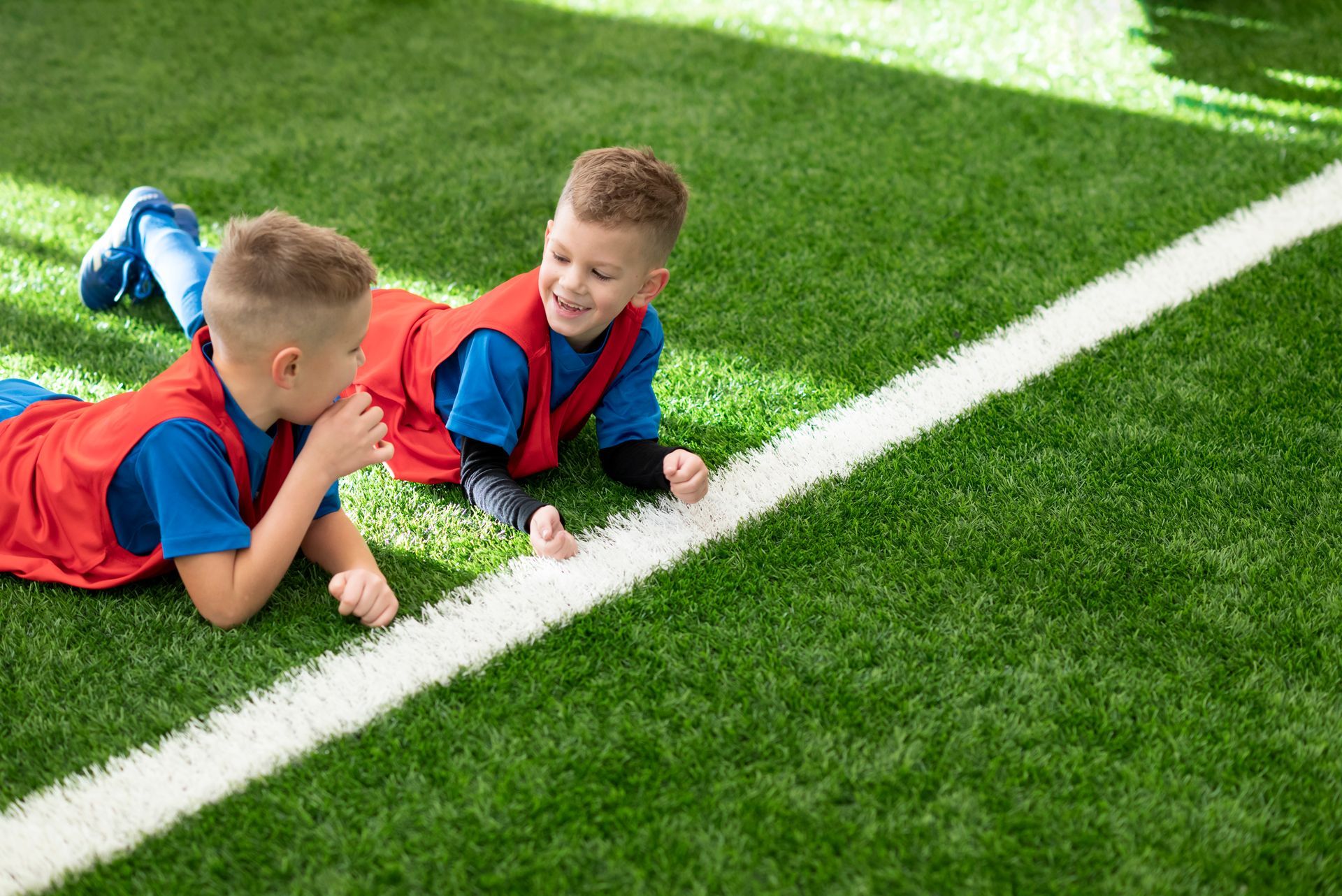Two young boys are laying on the grass on a soccer field.