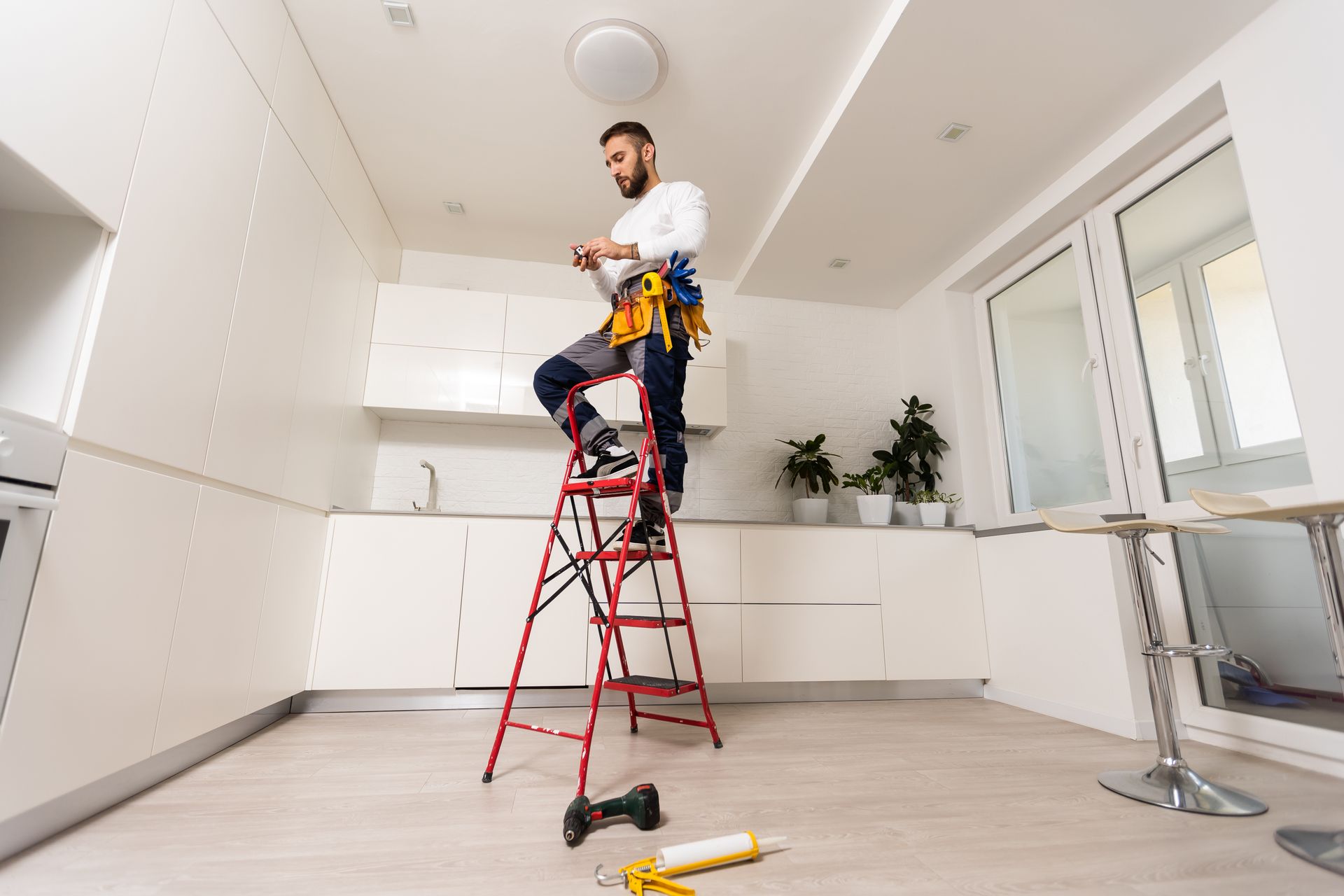 A man is standing on a ladder in a kitchen.
