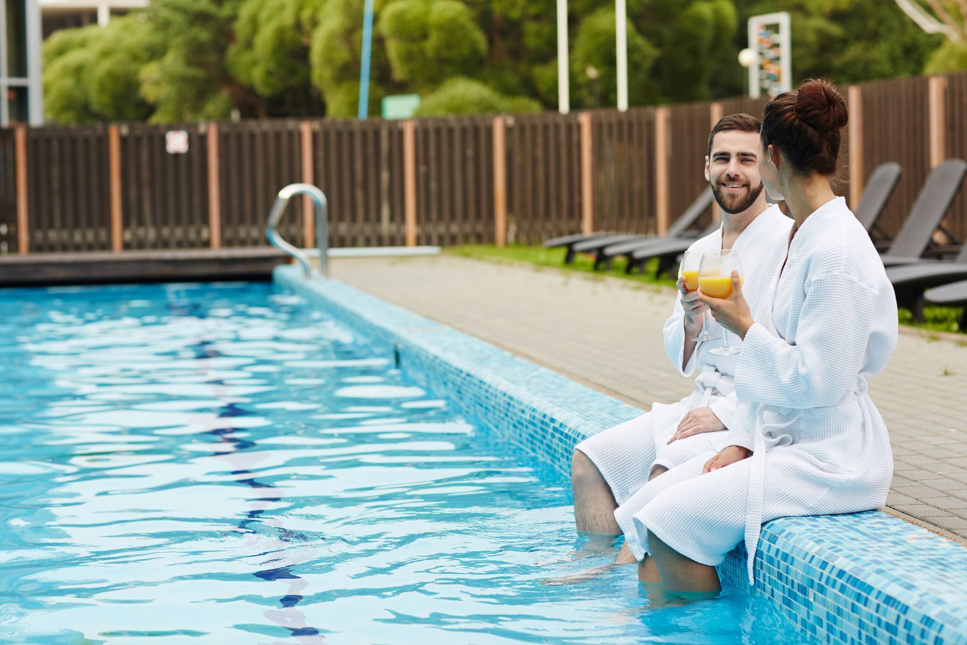 A man and a woman are sitting on the edge of a swimming pool.