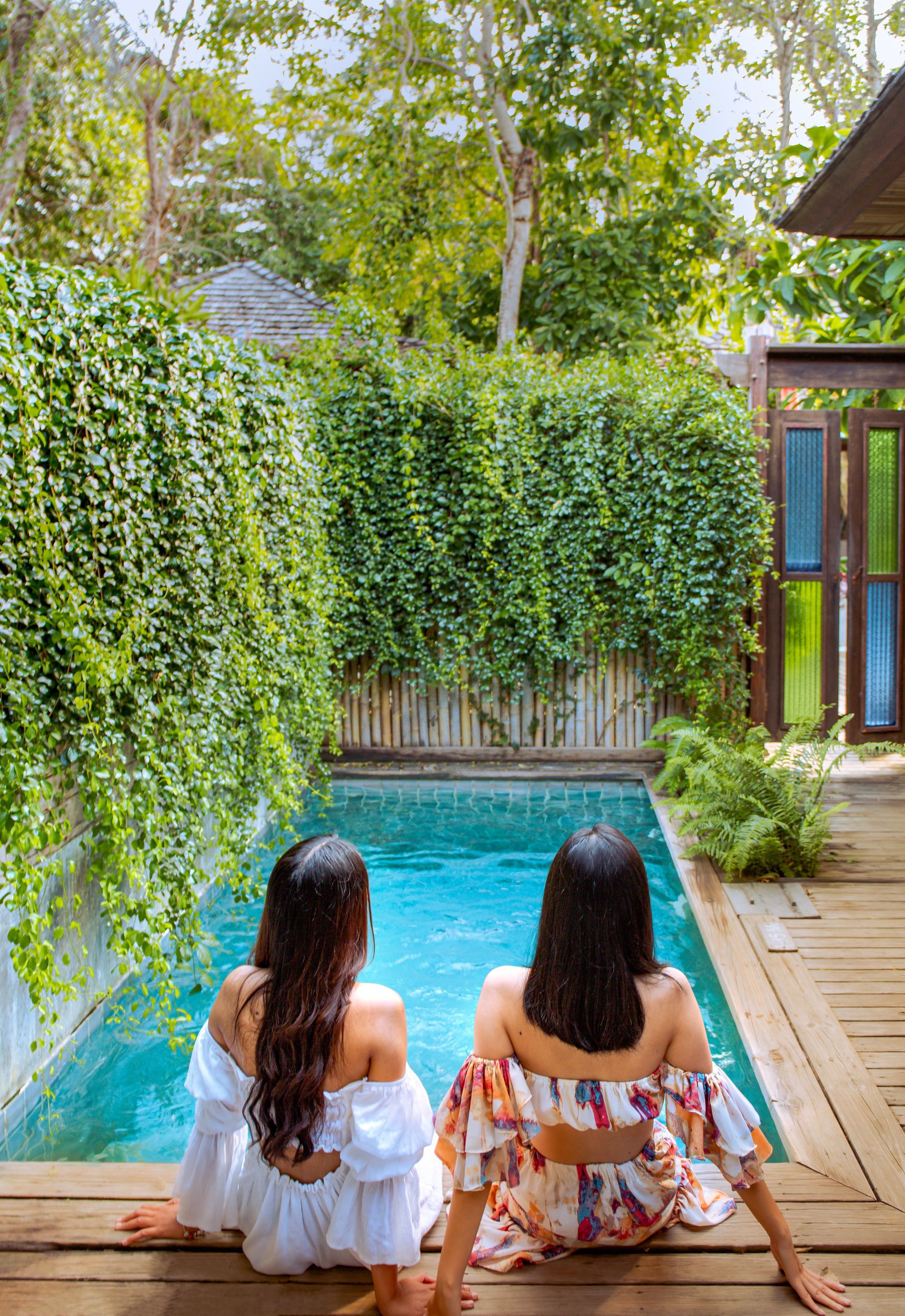 Two women are sitting on a wooden deck next to a swimming pool.