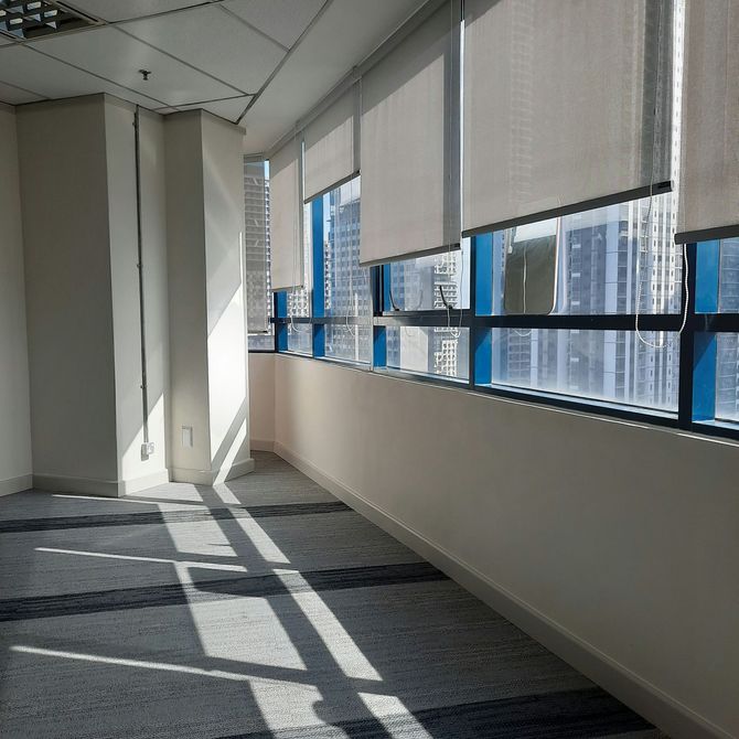 Sunlit office hallway with carpet, white walls, and large windows with blinds overlooking city buildings