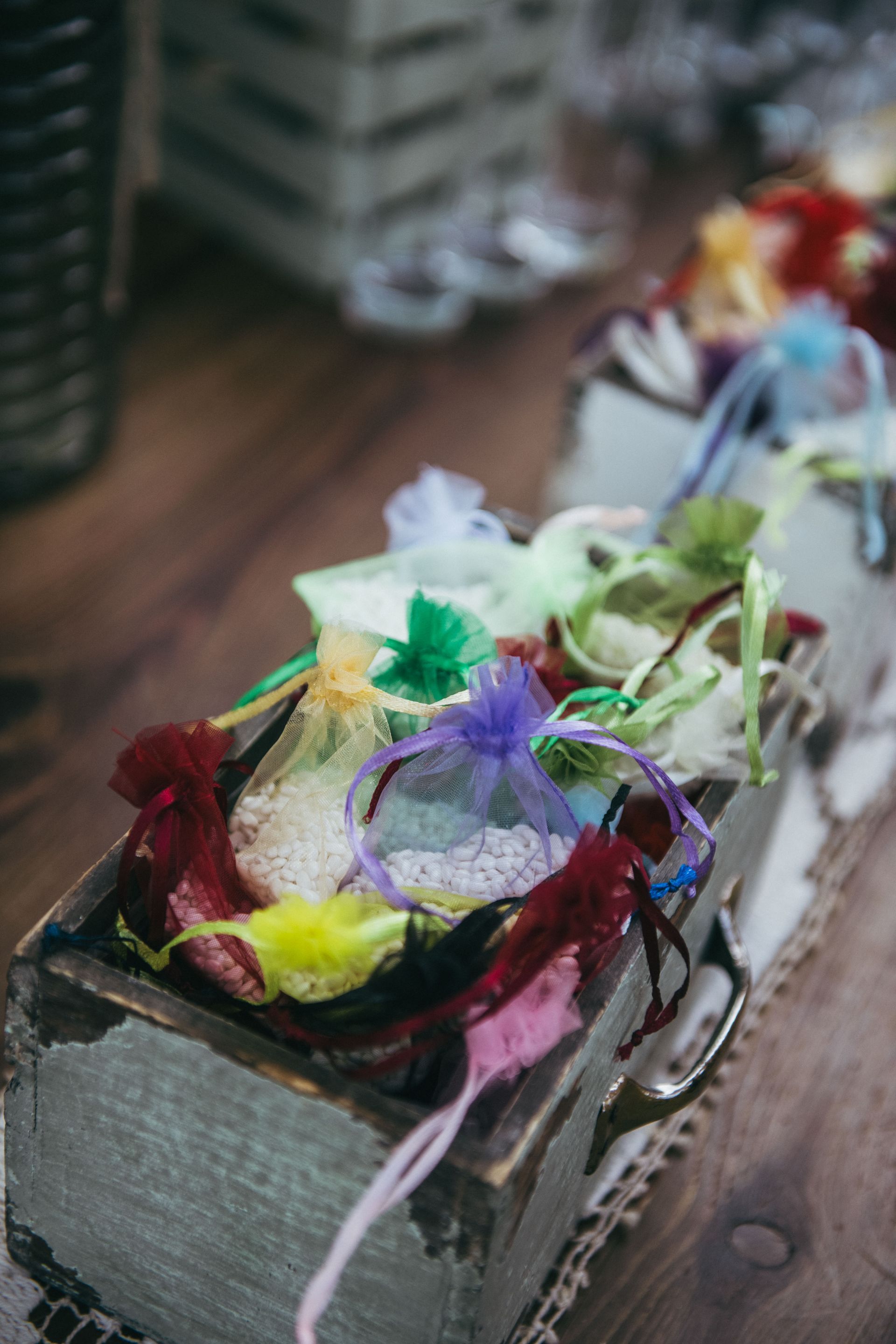 Scatola di legno piena di sacchetti di organza colorati legati con nastri, esposti su una superficie di legno.