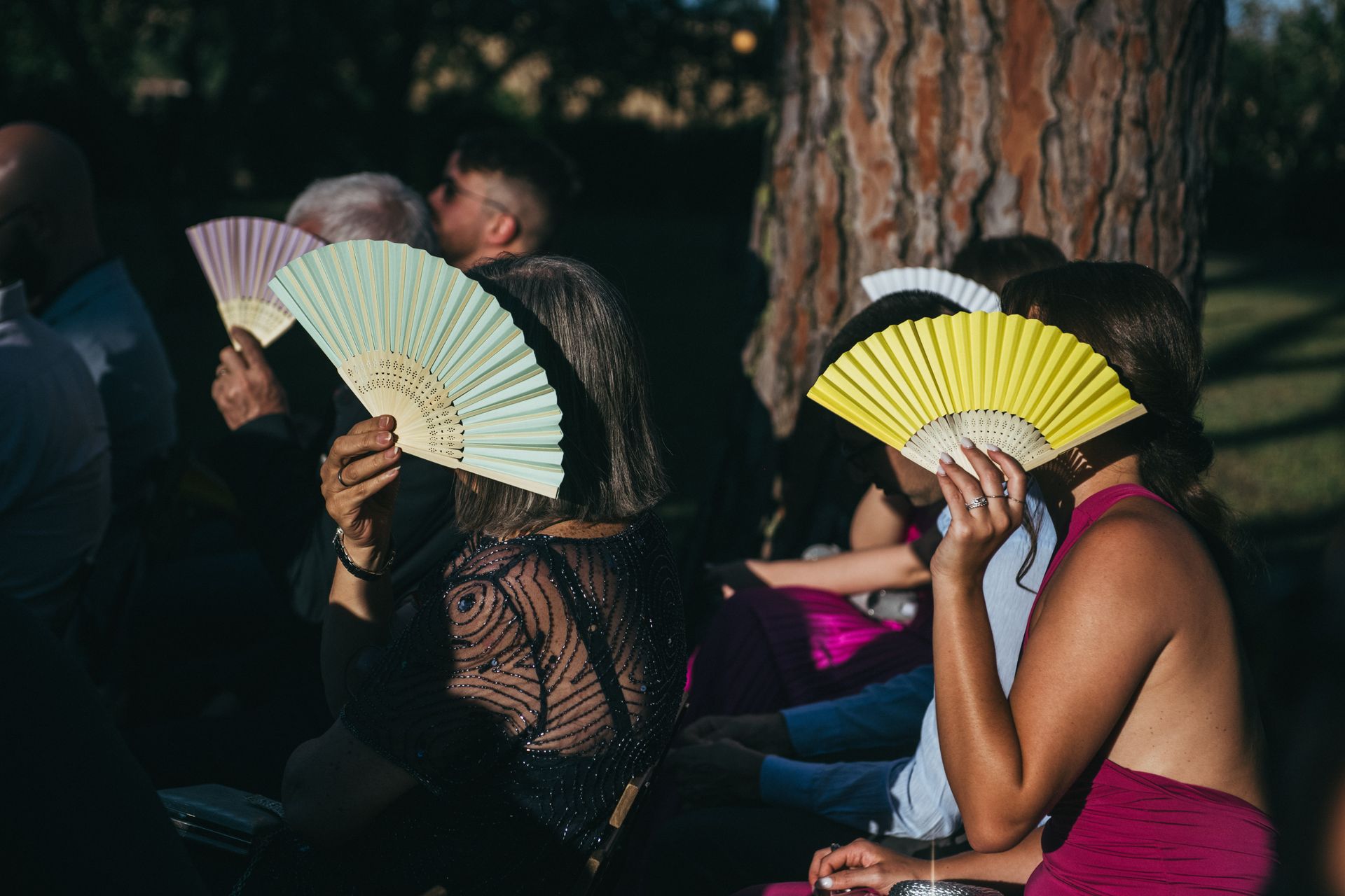 Le persone usano i ventagli colorati all'aperto, sotto un albero, magari durante una cerimonia.