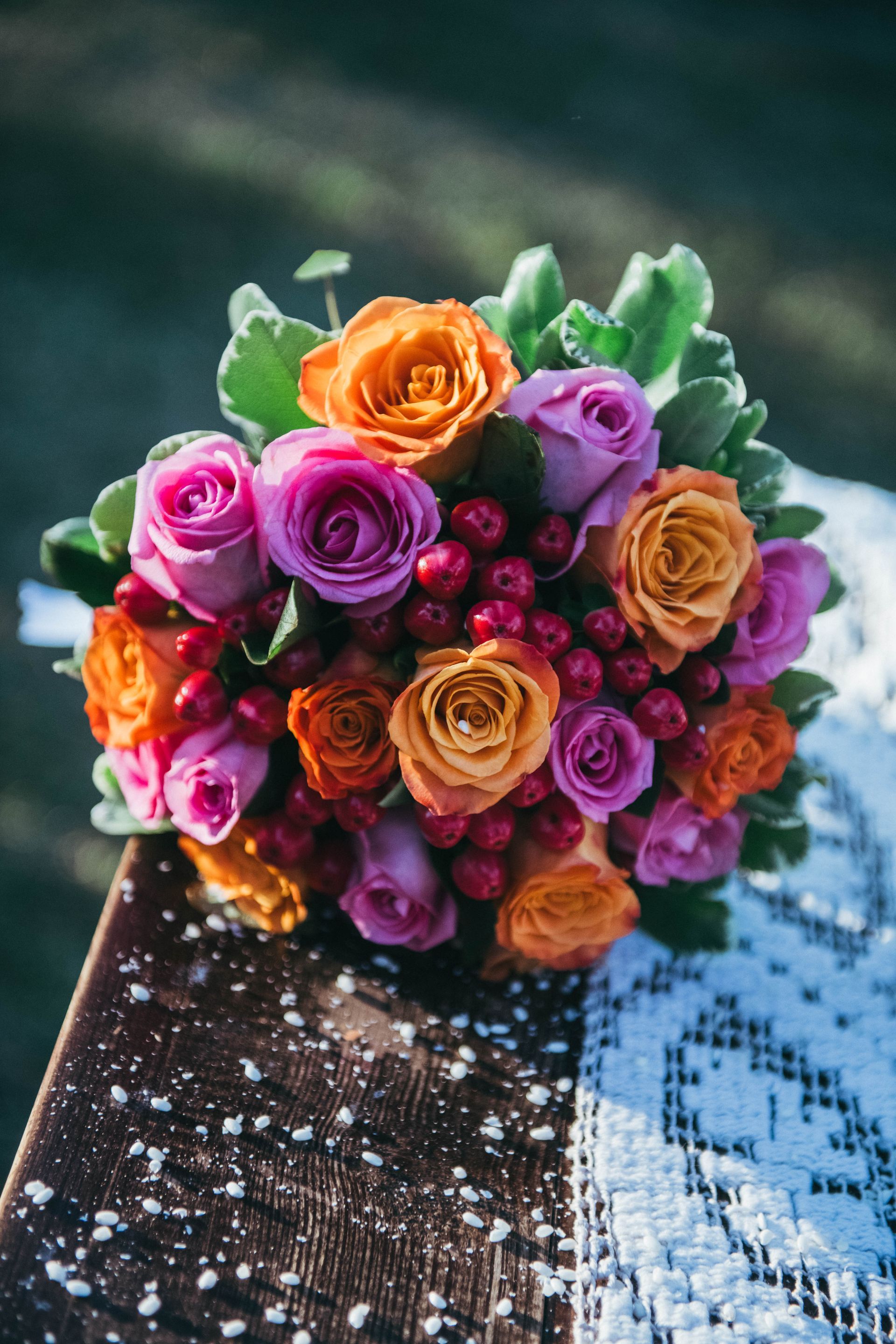 Bouquet di rose arancioni e rosa con bacche rosse, su una superficie di legno con pizzo.