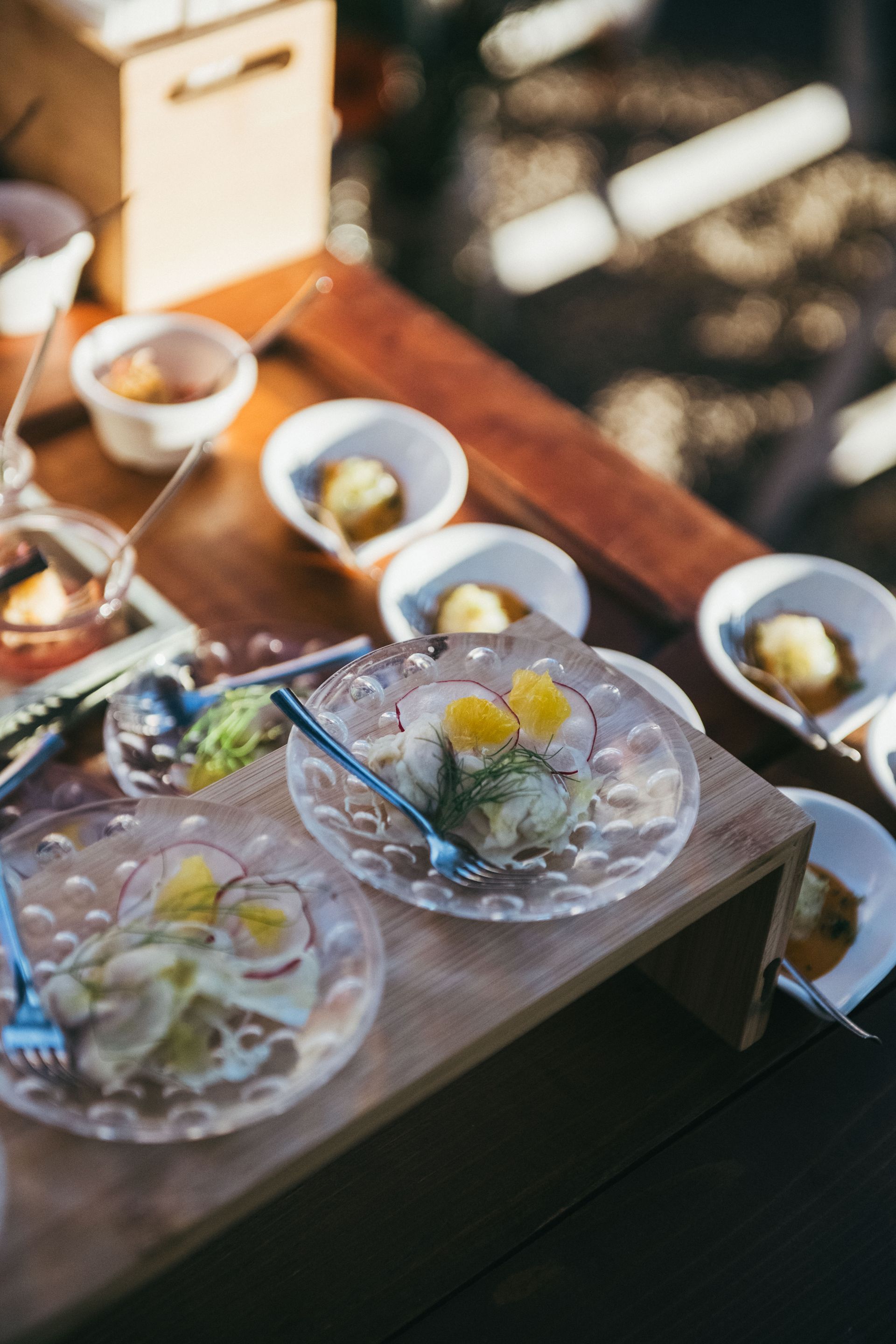 Piccoli piatti di antipasti con fette d'arancia su un tagliere di legno, all'aperto.