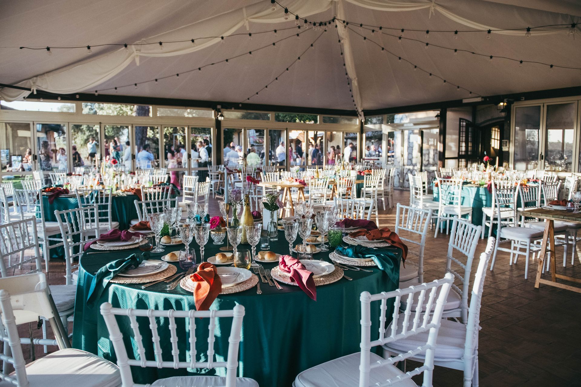 Ricevimento di nozze: tavoli rotondi con tovaglie color verde acqua, sedie bianche e centrotavola all'interno di una tenda.