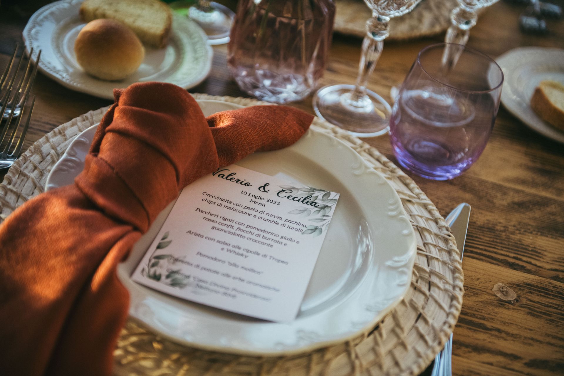 Apparecchiatura: piatto, tovagliolo, menù, pane, bicchieri su un tavolo di legno.