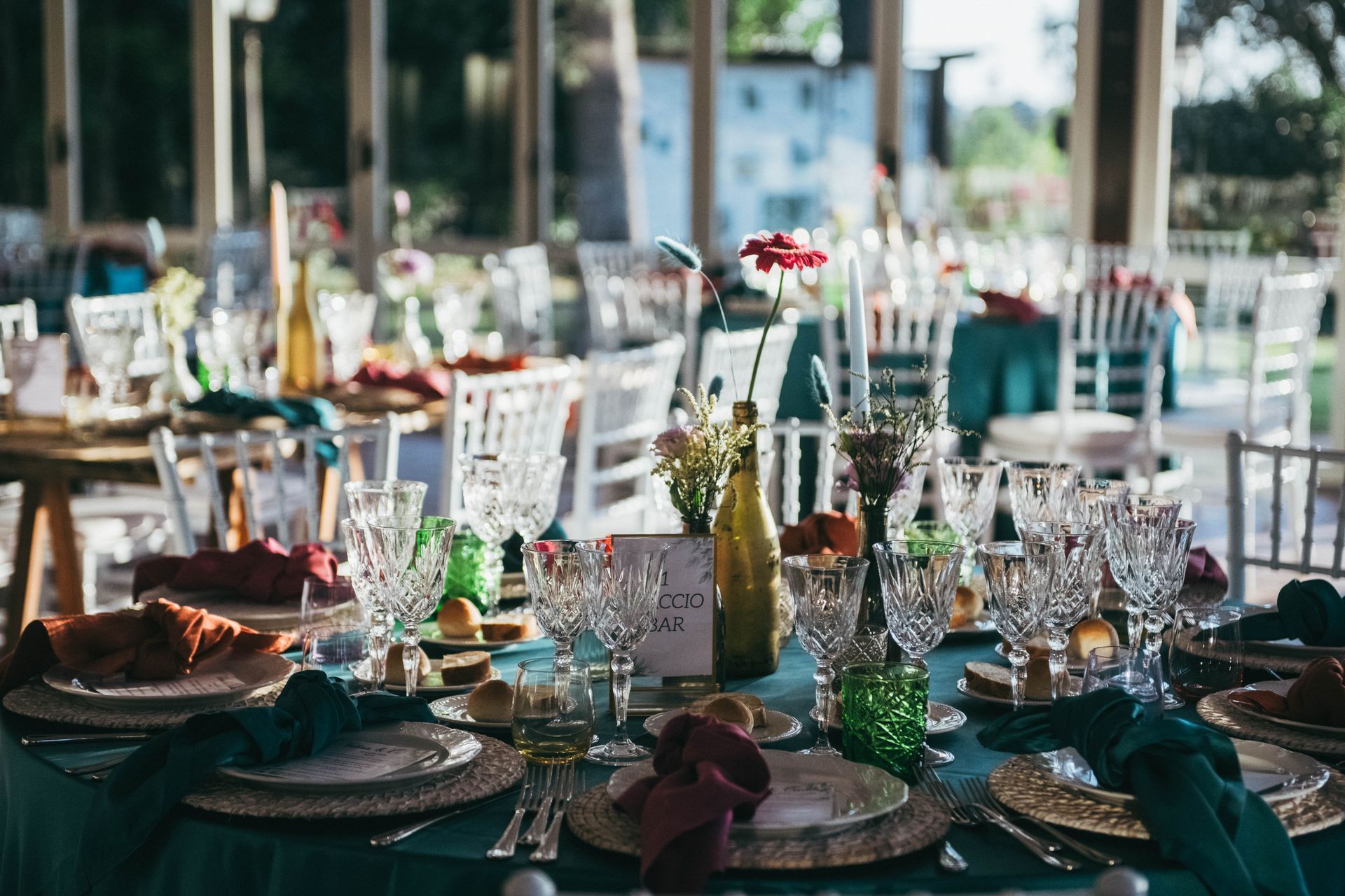 Elegante tavolo da pranzo apparecchiato per una festa, con tovaglia verde acqua, bicchieri decorati e centrotavola floreali.