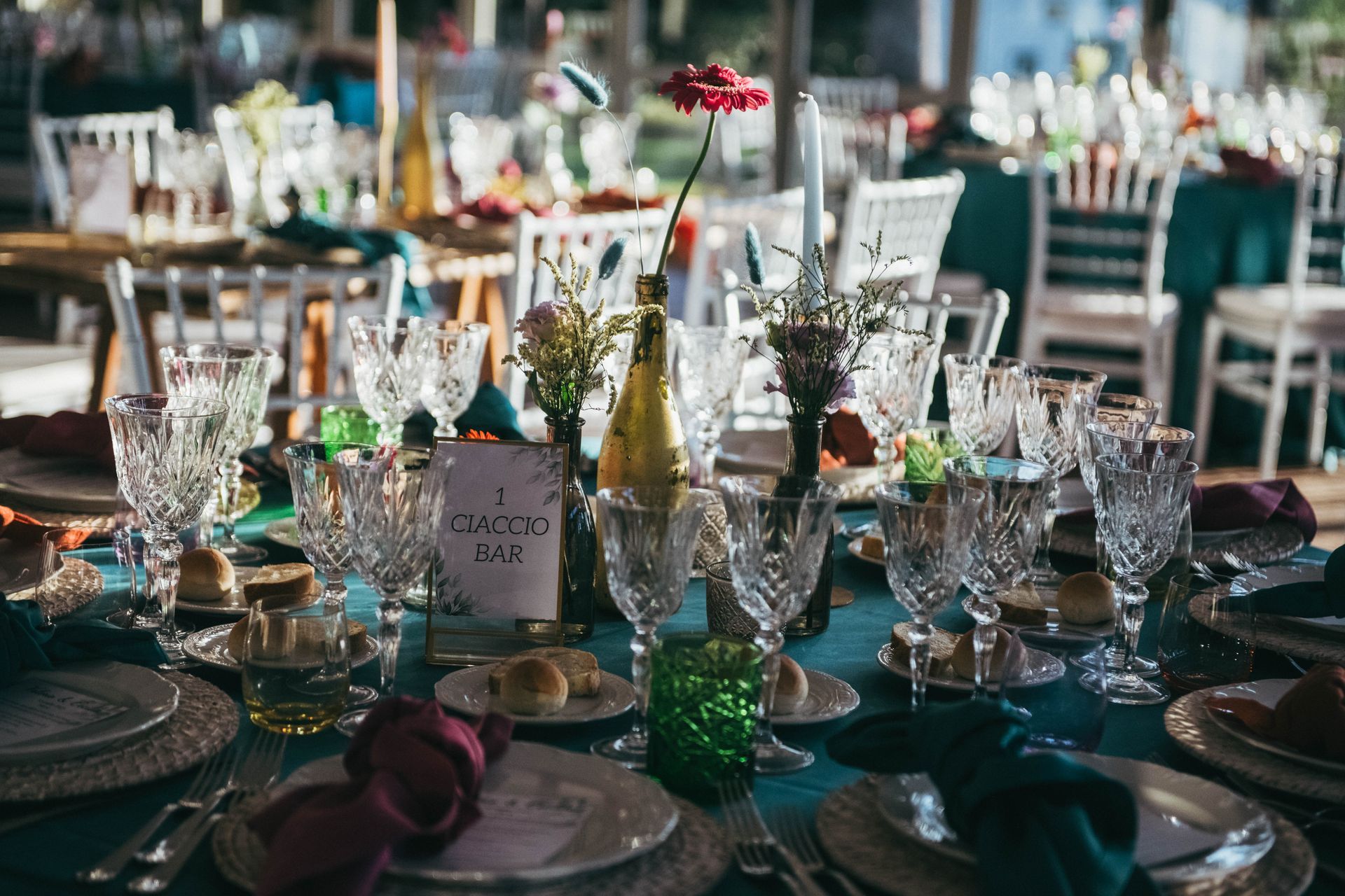 Tavolo da pranzo festivo rivestito in verde acqua, apparecchiato con eleganti bicchieri, fiori e posate.