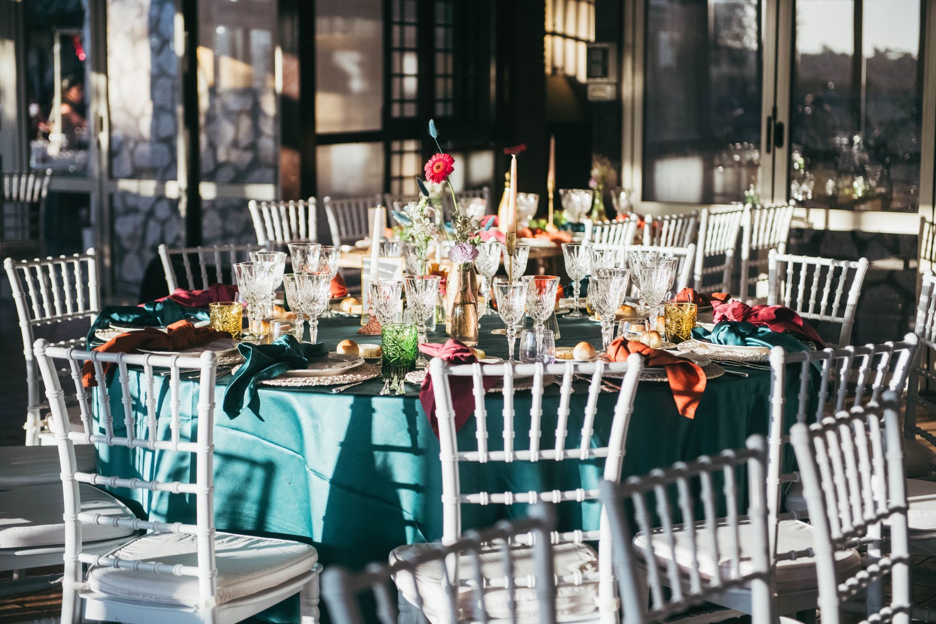 Tavolo rotondo apparecchiato per una festa, tovaglia verde acqua, sedie bianche.
