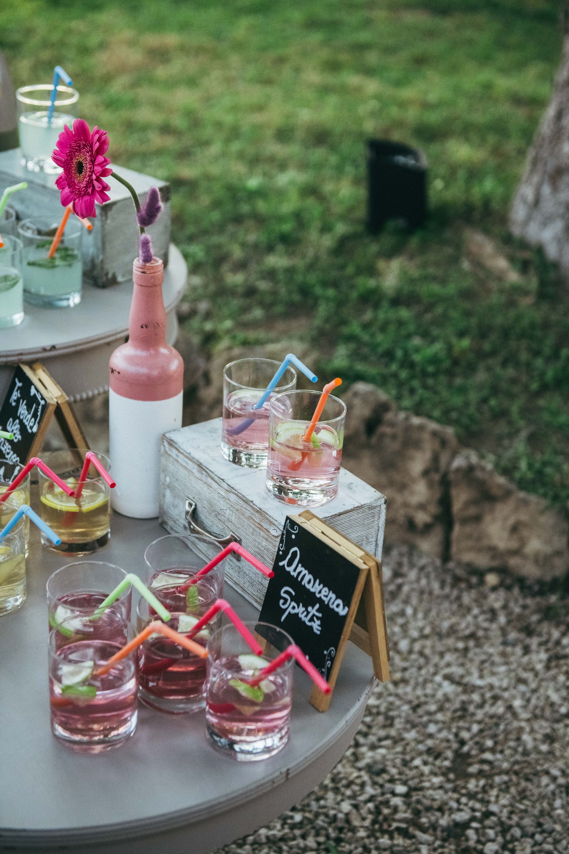 Tavolo da cocktail con bevande, cannucce e fiori in un ambiente esterno.