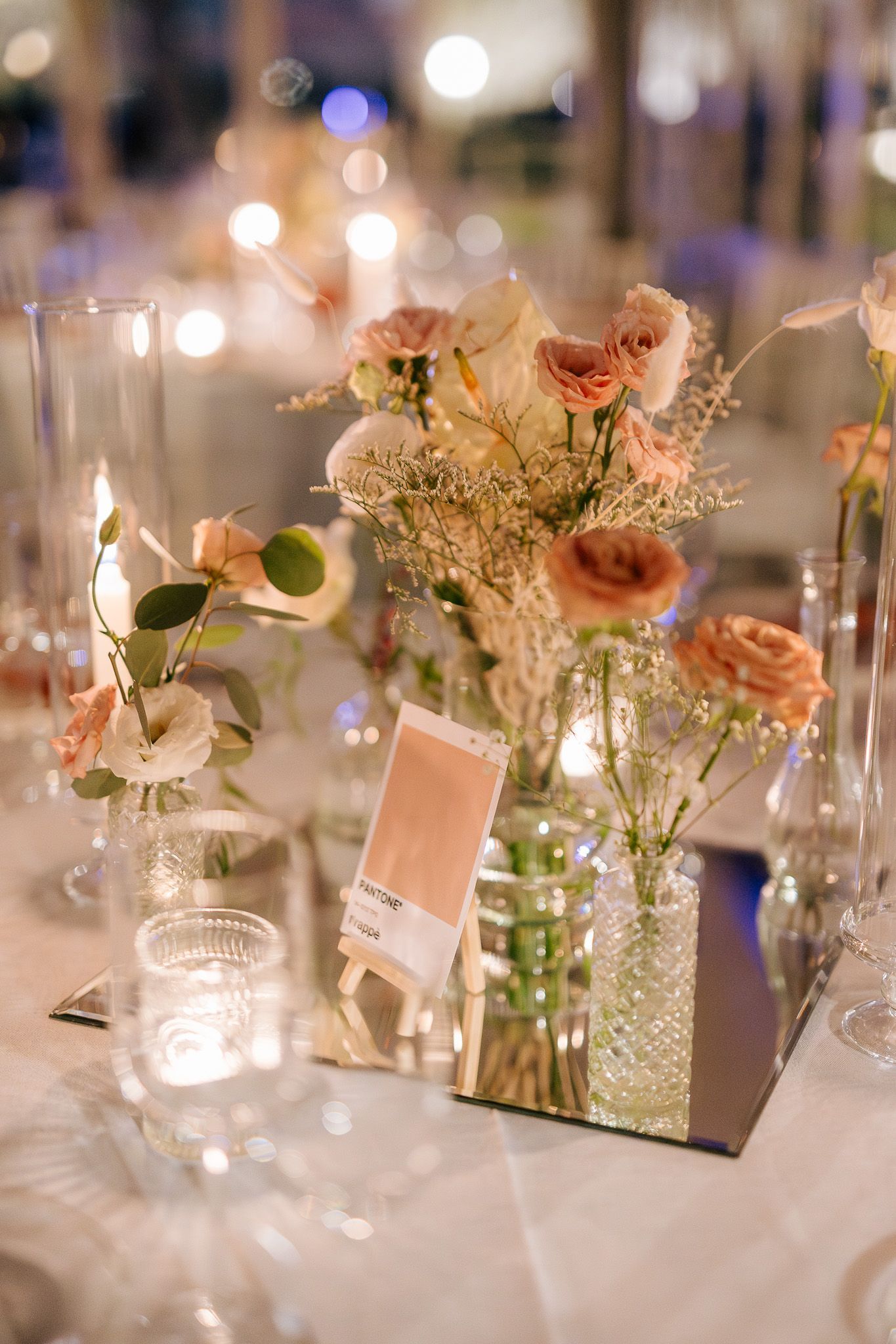 Centrotavola nuziale con fiori e candele, riflessi su uno specchio.