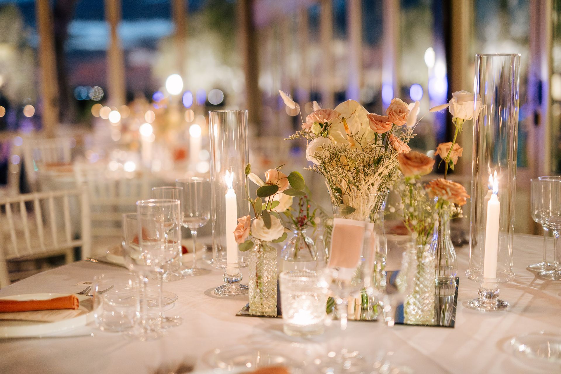 Elegante apparecchiatura della tavola con centrotavola floreali, candele e bicchieri per un evento serale.