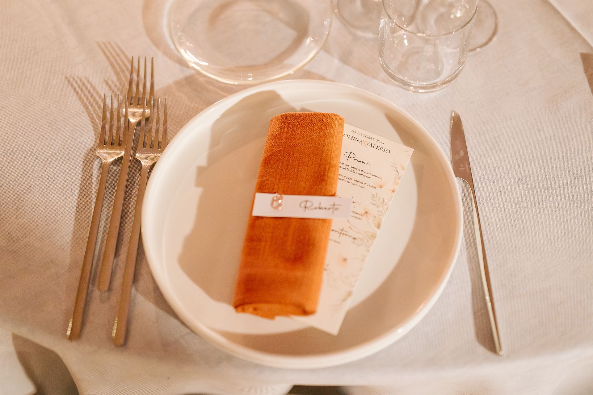 Apparecchiatura formale del tavolo con tovagliolo arancione su un piatto bianco, posate e bicchieri per l'acqua.