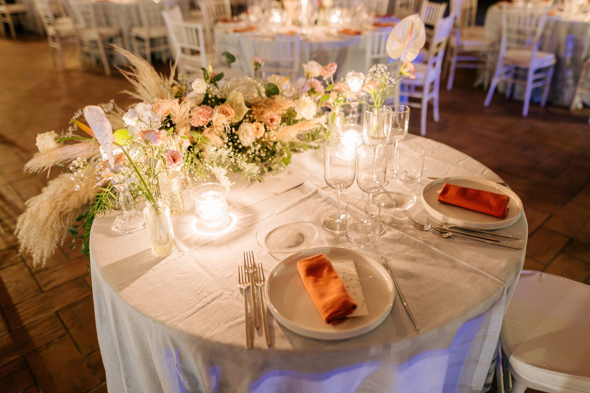 Tavolo per il ricevimento di nozze con centrotavola floreale, candele e apparecchiato per la tavola.