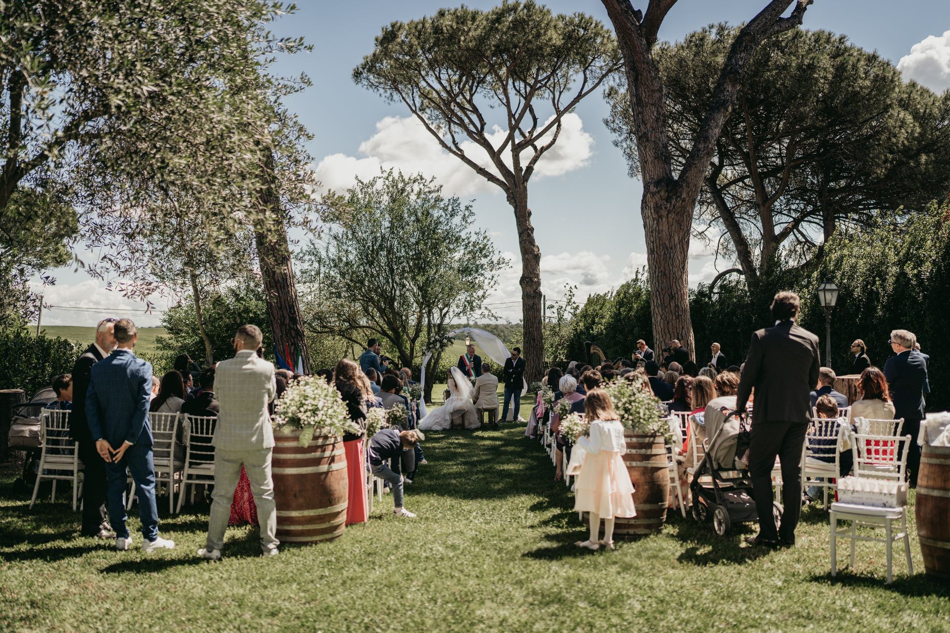 Cerimonia nuziale all'aperto con invitati e sposi sotto gli alberi.