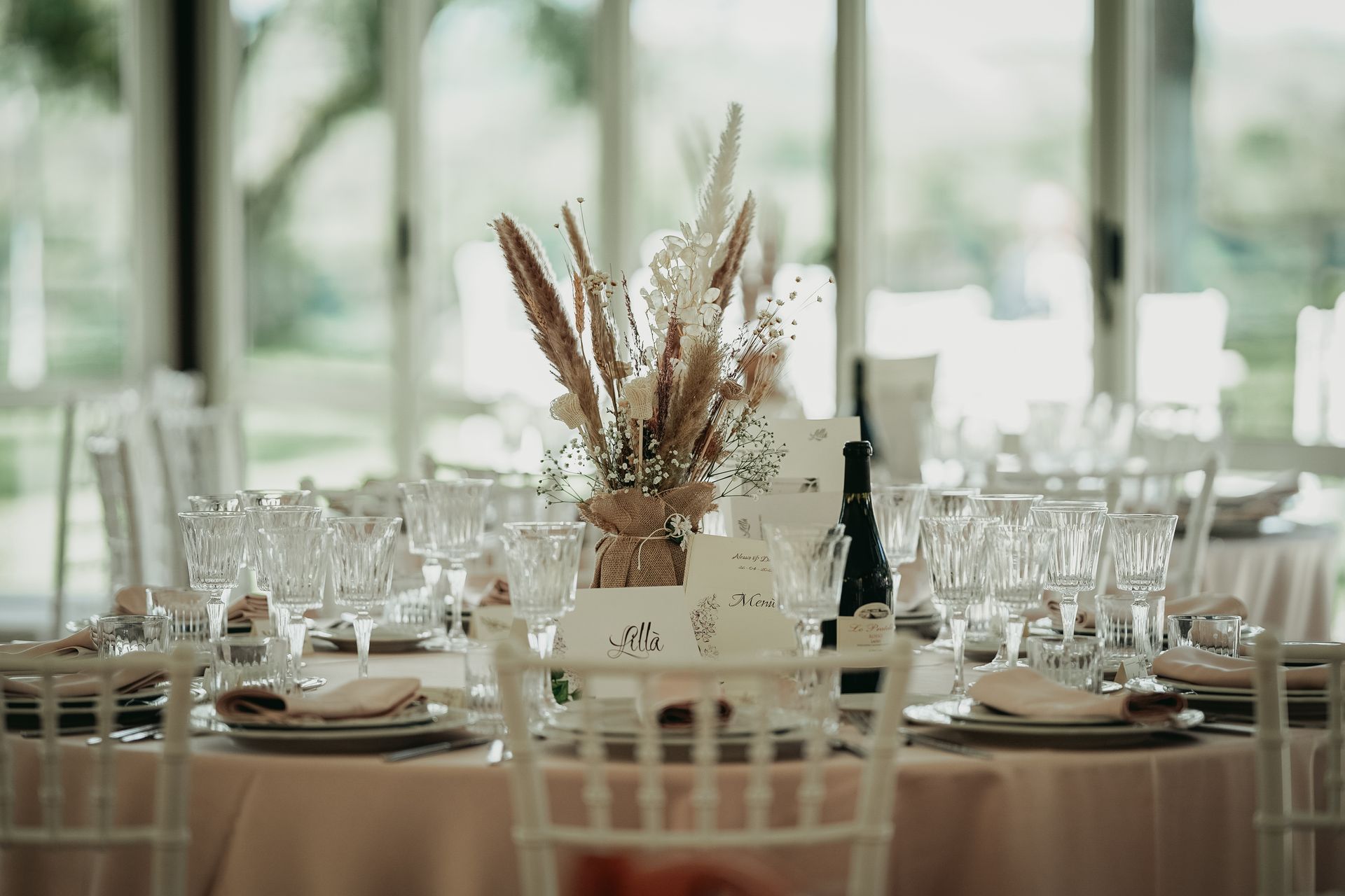 Tavolo per il ricevimento di nozze apparecchiato con centrotavola floreale, bicchieri e posate.