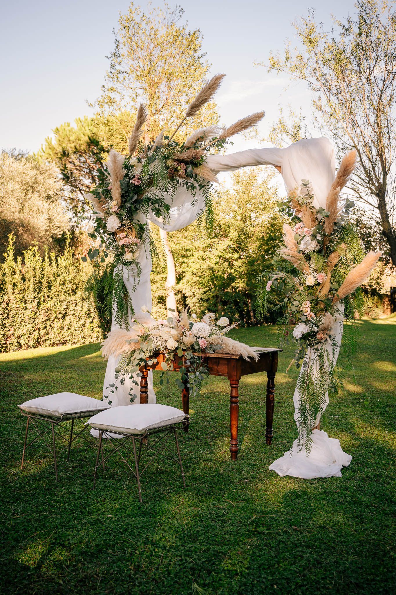 Allestimento per cerimonia nuziale con arco floreale e tavolo su un prato.