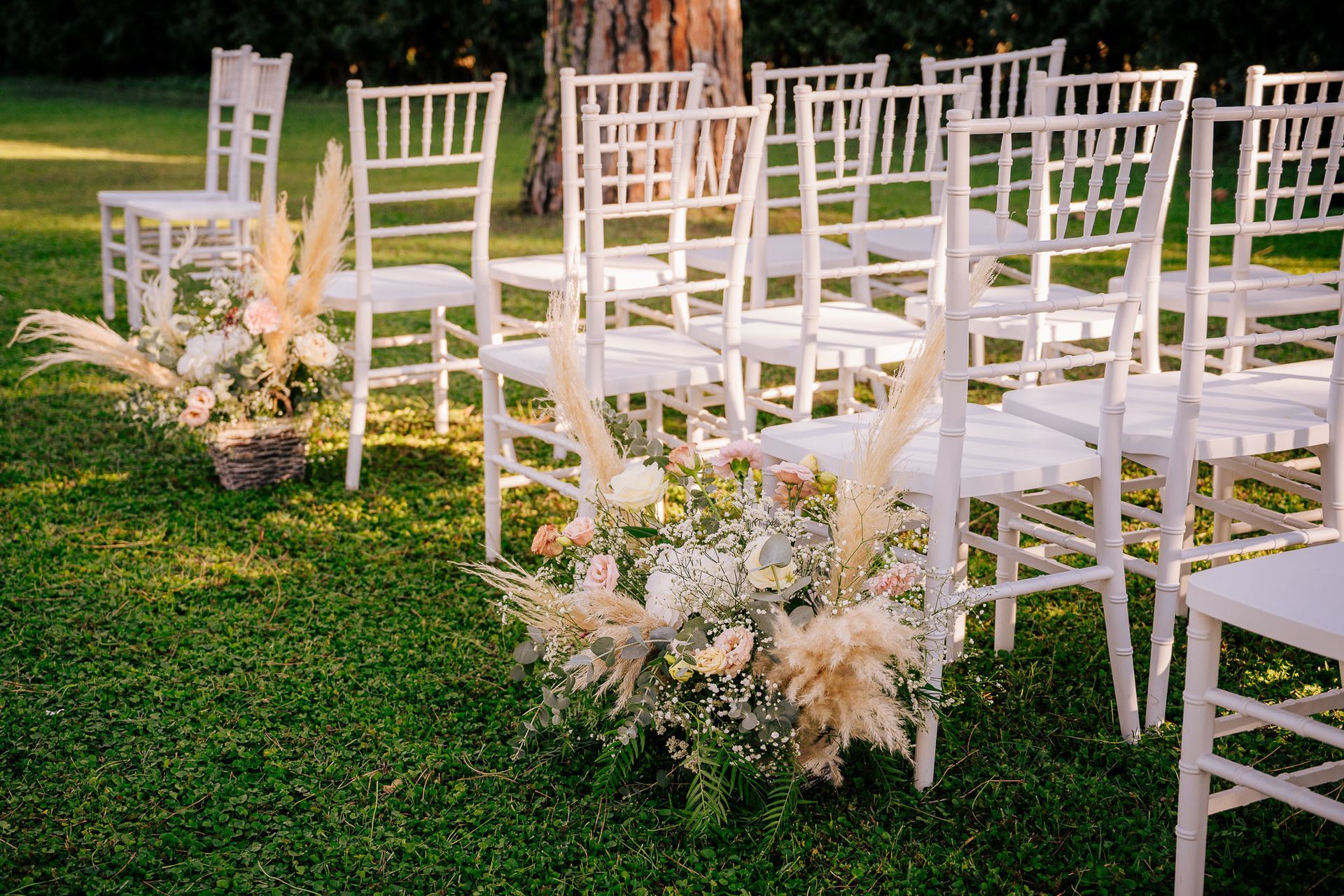 Sedie bianche disposte sull'erba con decorazioni floreali per un evento all'aperto.