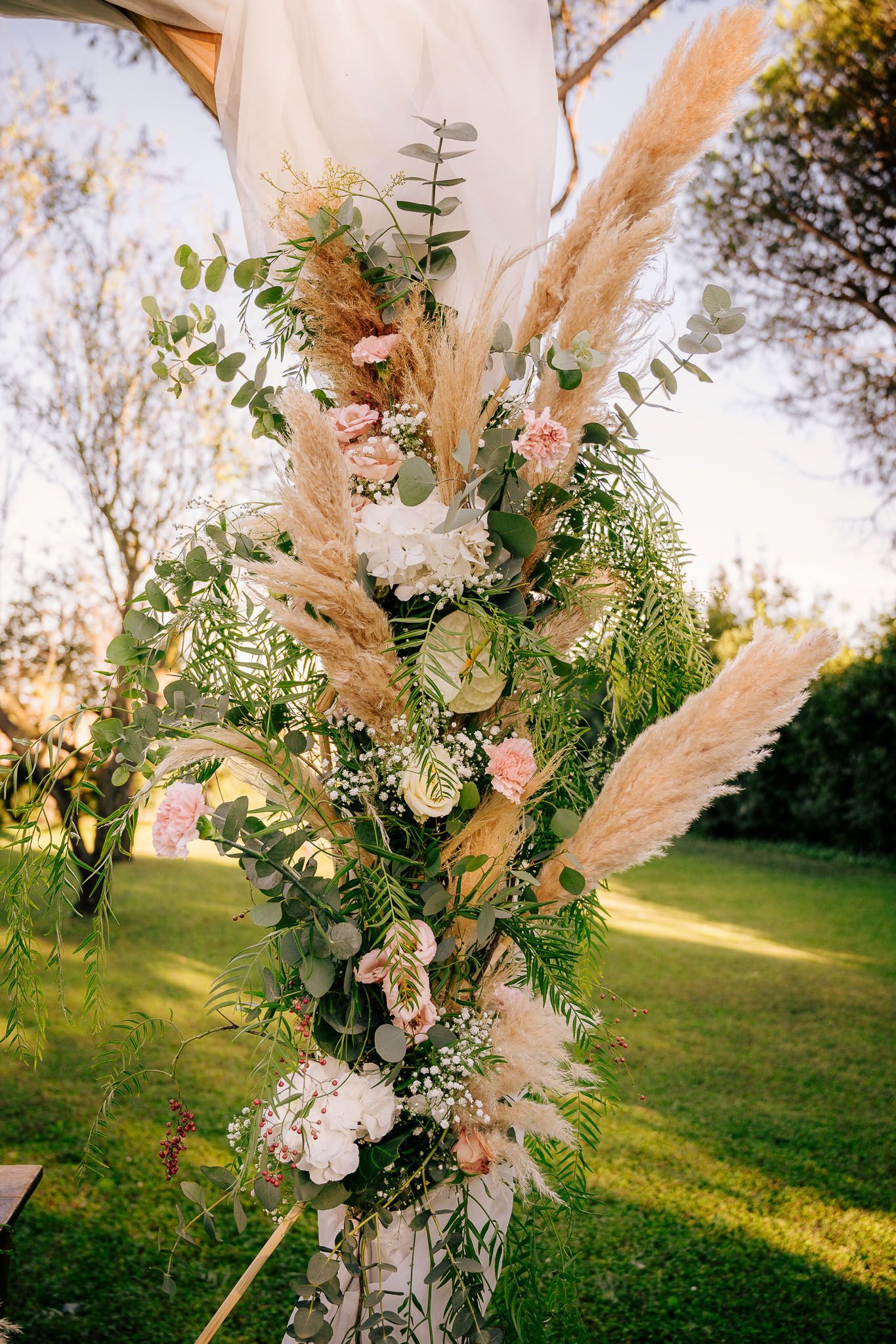 Arco nuziale con erba della pampa, eucalipto e fiori bianchi e rosa. Allestito all'aperto in giardino.