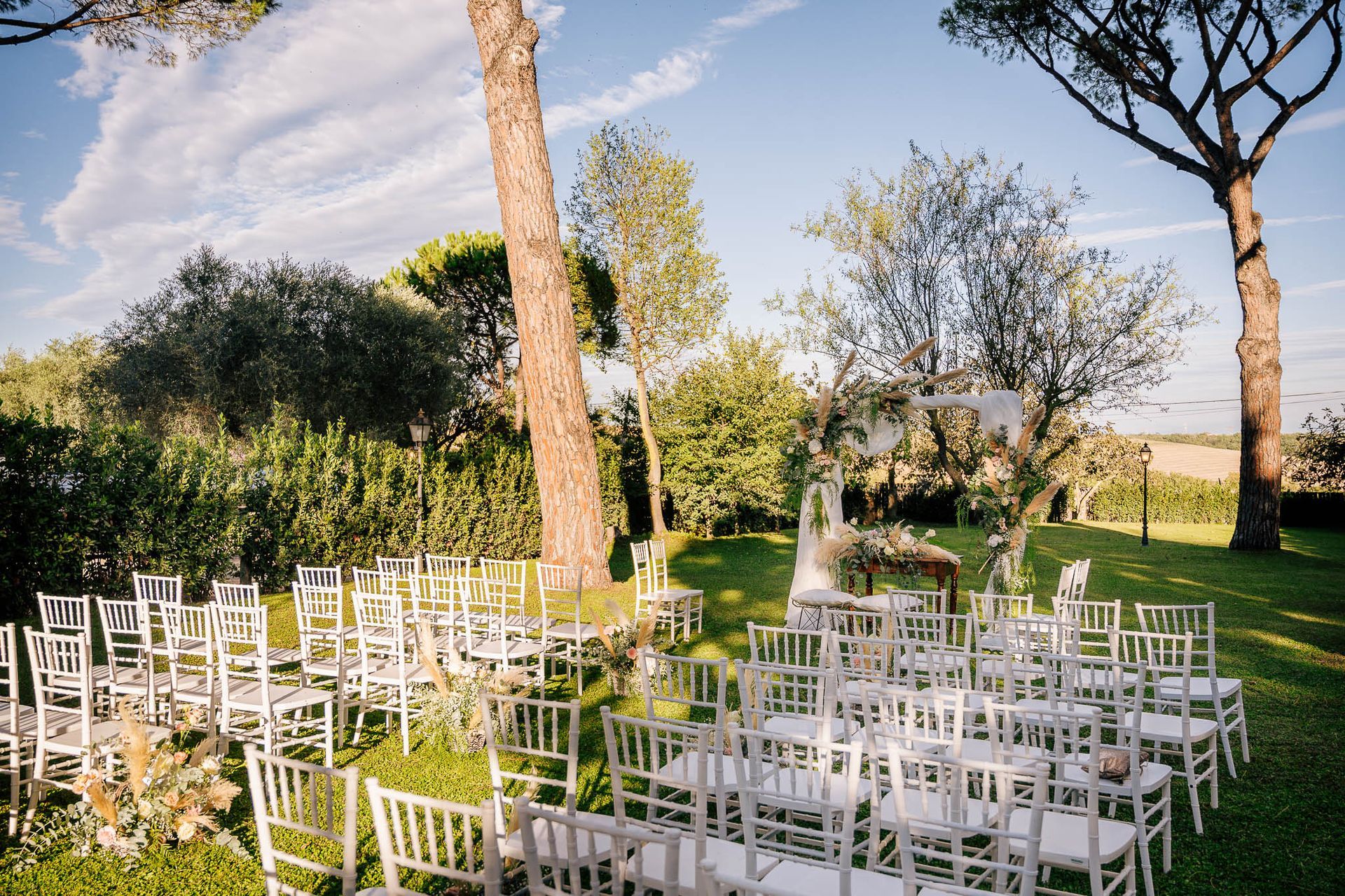 Cerimonia nuziale all'aperto con sedie bianche su un prato verde. Arco decorato con fiori.