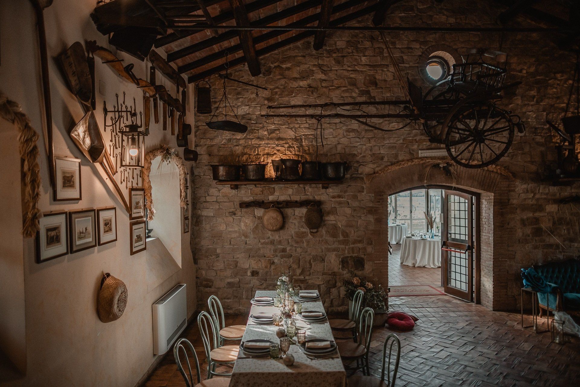 Lungo tavolo da pranzo sistemato in una stanza in pietra, che conduce a una porta, decorata con pezzi d'antiquariato.
